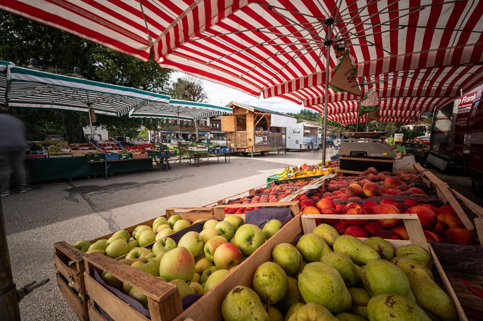 Etliche Marktstände in Fischen, Am Anger, mit Obst und Gemüse unter rot-weiß gestreiften Schirmen.