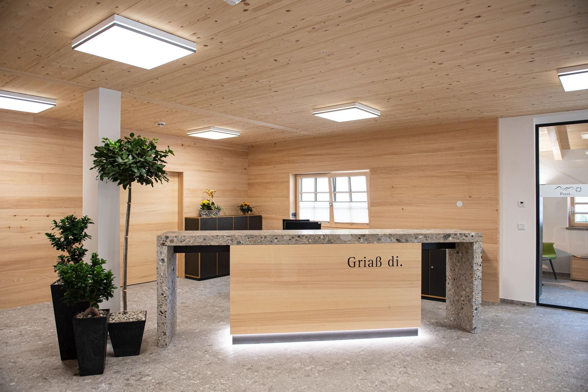 Heller Empfangsbereich im Dorfhaus Balderschwang. Rezeptionstheke mit Aufschrift "Griaß di." vor holzvertäfelter Wand.