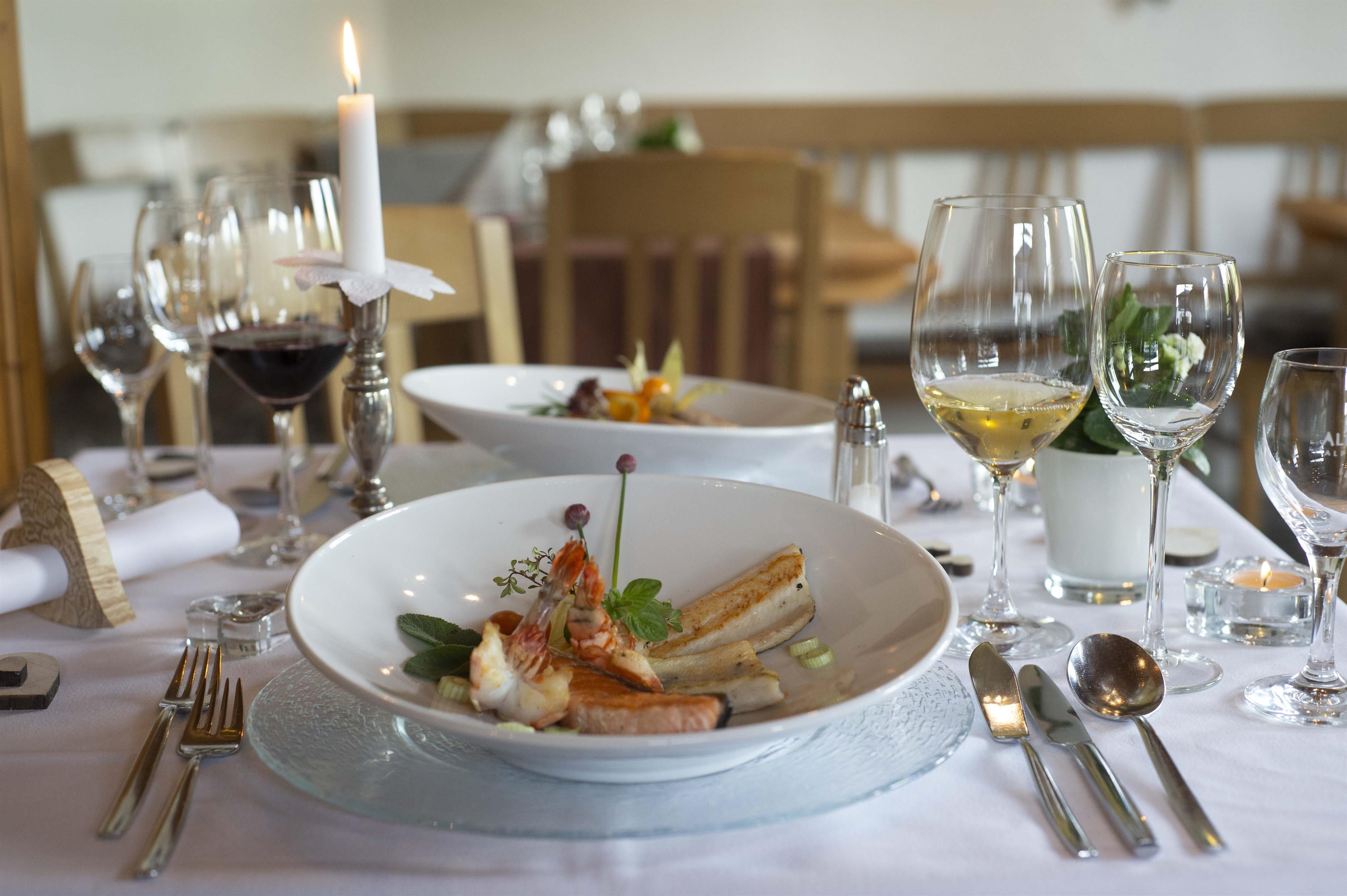 Weiß gedeckter Tisch für zwei Personen, verschiedene Gläser, silbernes Besteck, eine brennende Kerze.