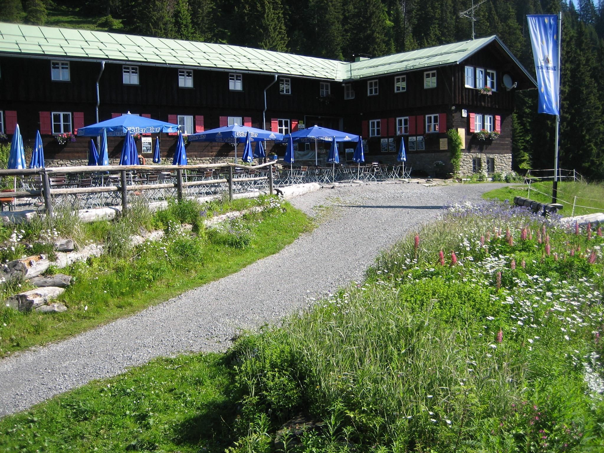 Berghaus Schwaben in Bolsterlang: Holzfassade, rote Fensterläden, Wiesenblick und Sitzplätze im Freien.