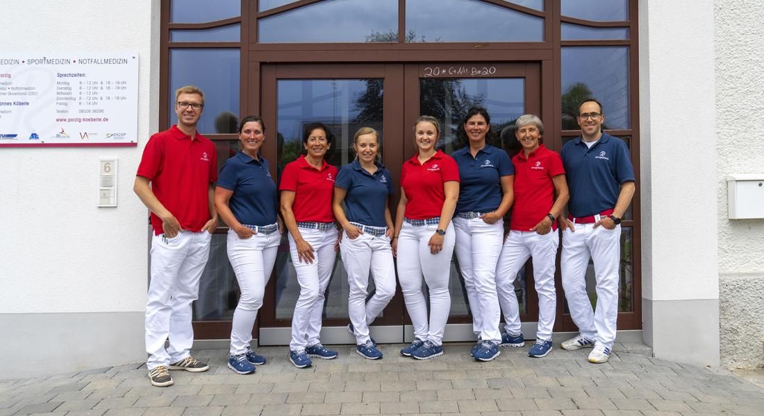 Das Praxisteam mit den Ärzten links und rechts, dazwischen ie Assistentinnen, Polo-Shirts rot und blau abwechselnd.