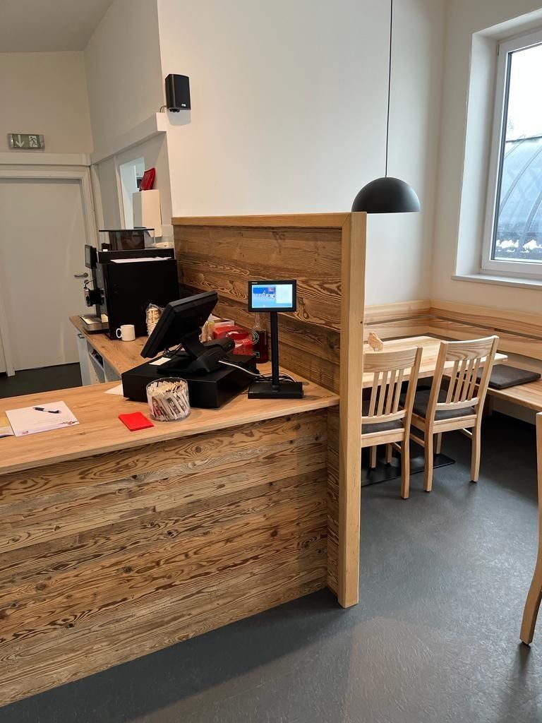 Die Theke ist aus Holz und mit einer Kasse und einer Kaffeemaschine ausgestattet.