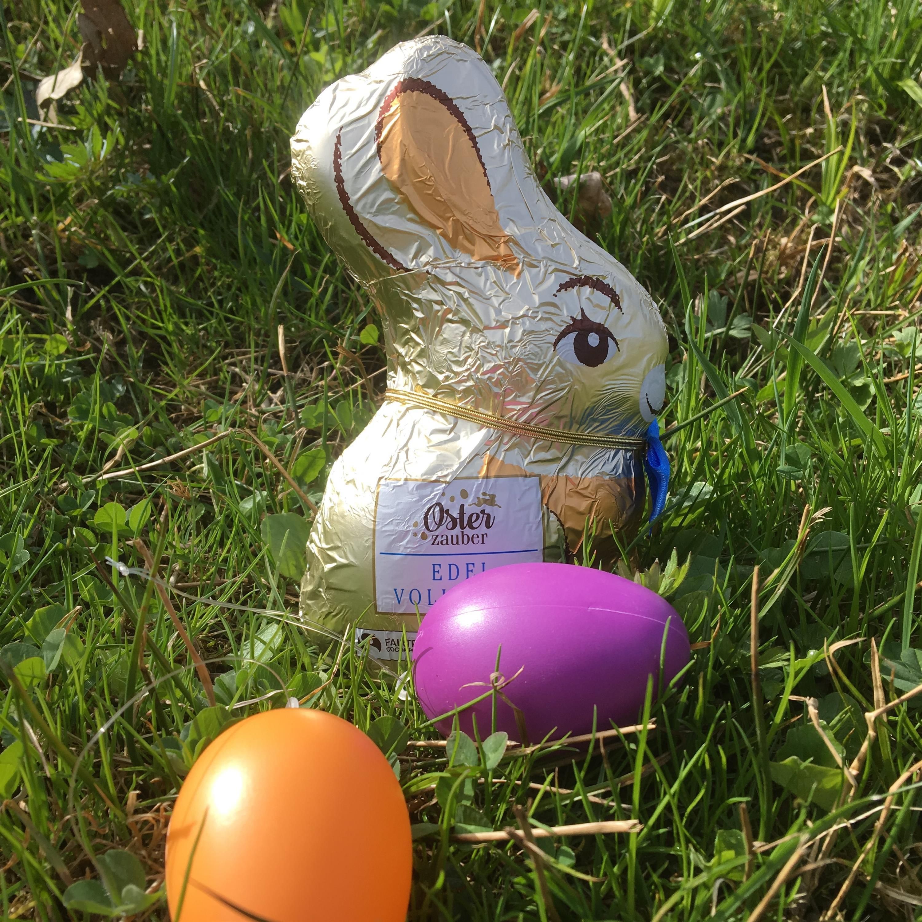 Ein goldener Schokoladenhase und zwei bunte Ostereier liegen in grünem Gras.
