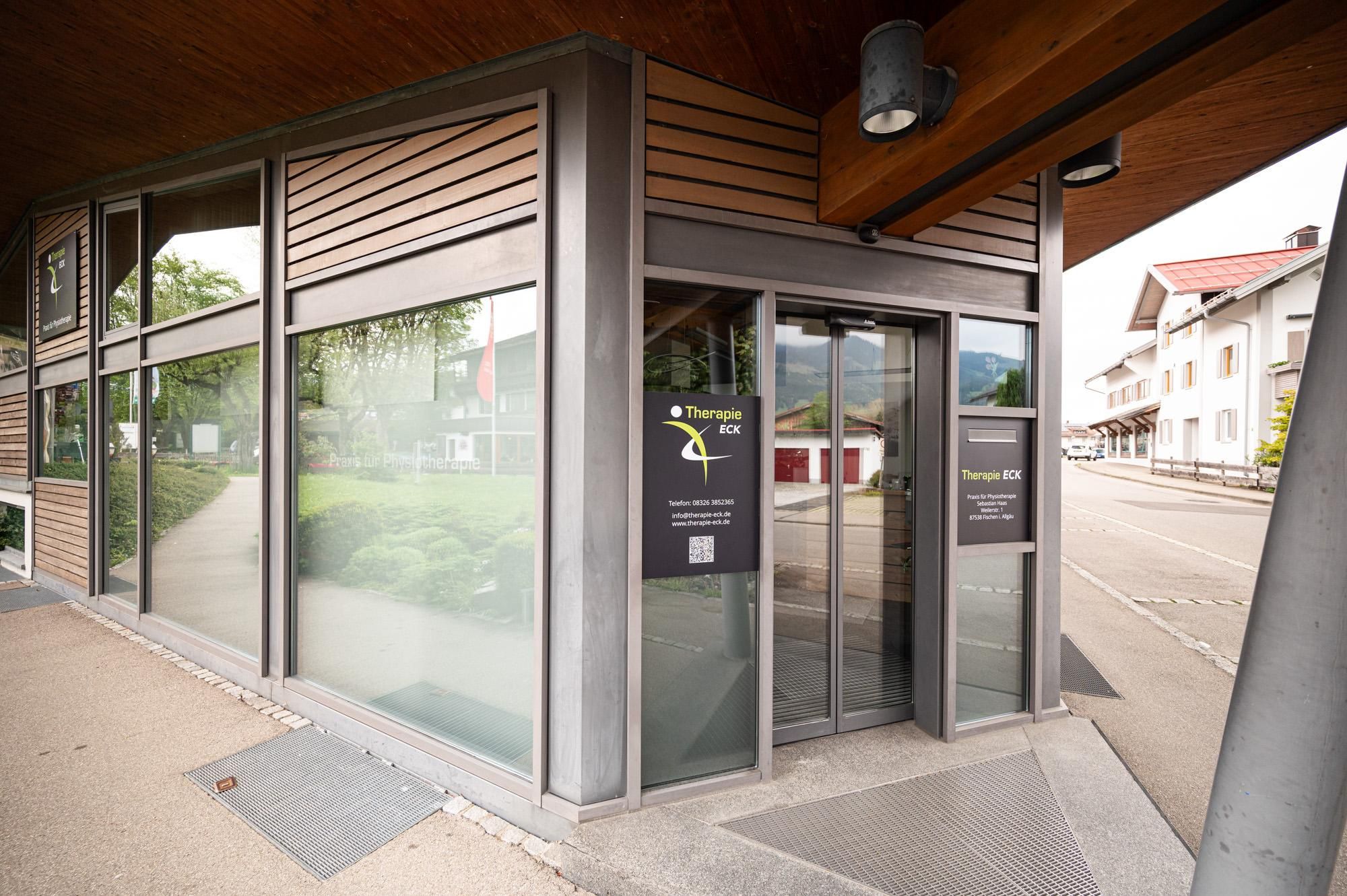 Der Eingang (nur eine Stufe) zur Physiotherapie "Therapie-Eck" in der Weilerstraße 1 in Fischen mit Schiebetür aus Glas.