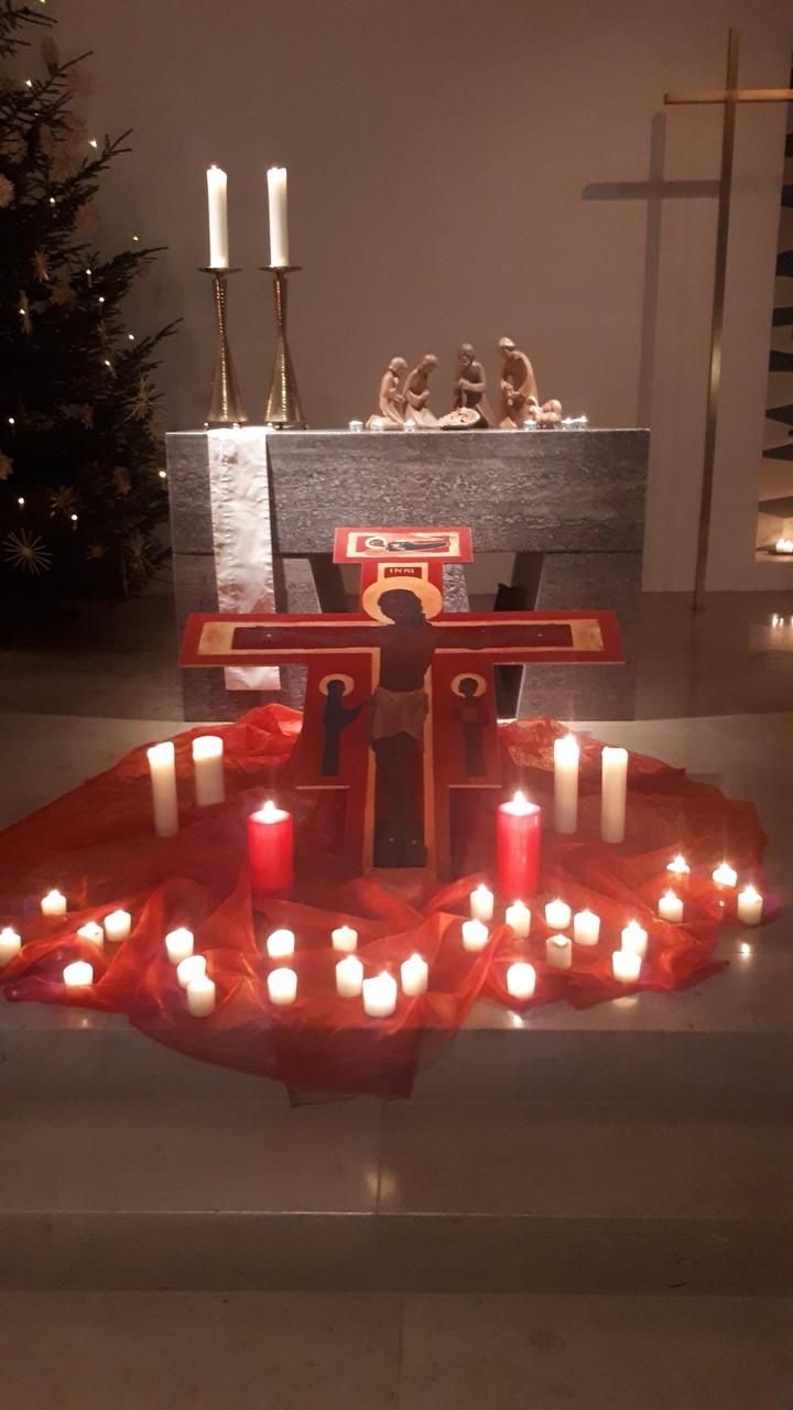 Dekoration vor dem Altar mit Kreuz und vielen Kerzen und Lichtern auf einer roten Decke.