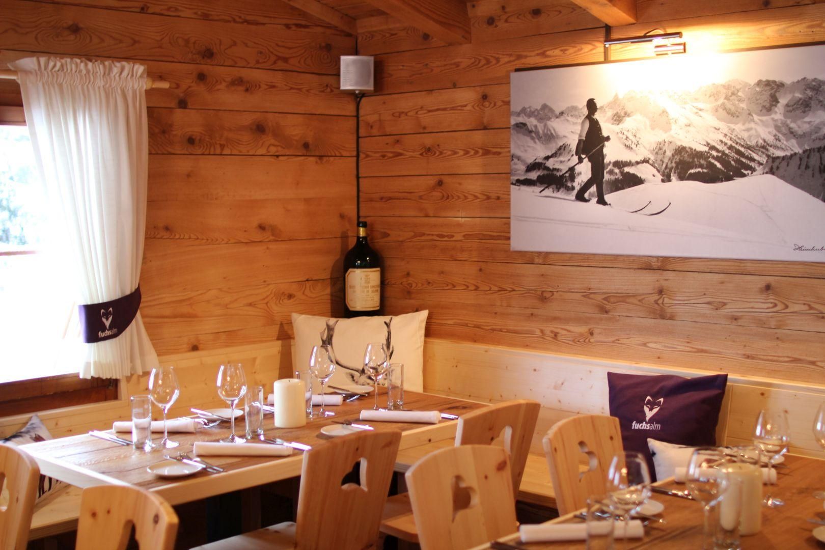 Hölzerne Almhütte der Fuchsalm in Balderschwang. Kleine Fenster mit rot-weiß karierten Vorhängen.