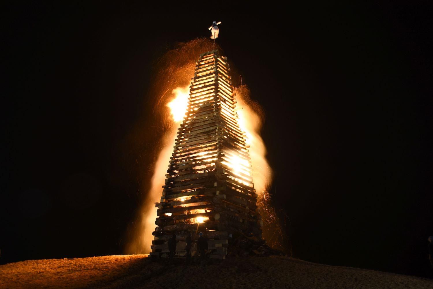 Turmartiges Holzscheit-Feuer lodert in der dunklen Nacht, Flammen und Funken wehen.