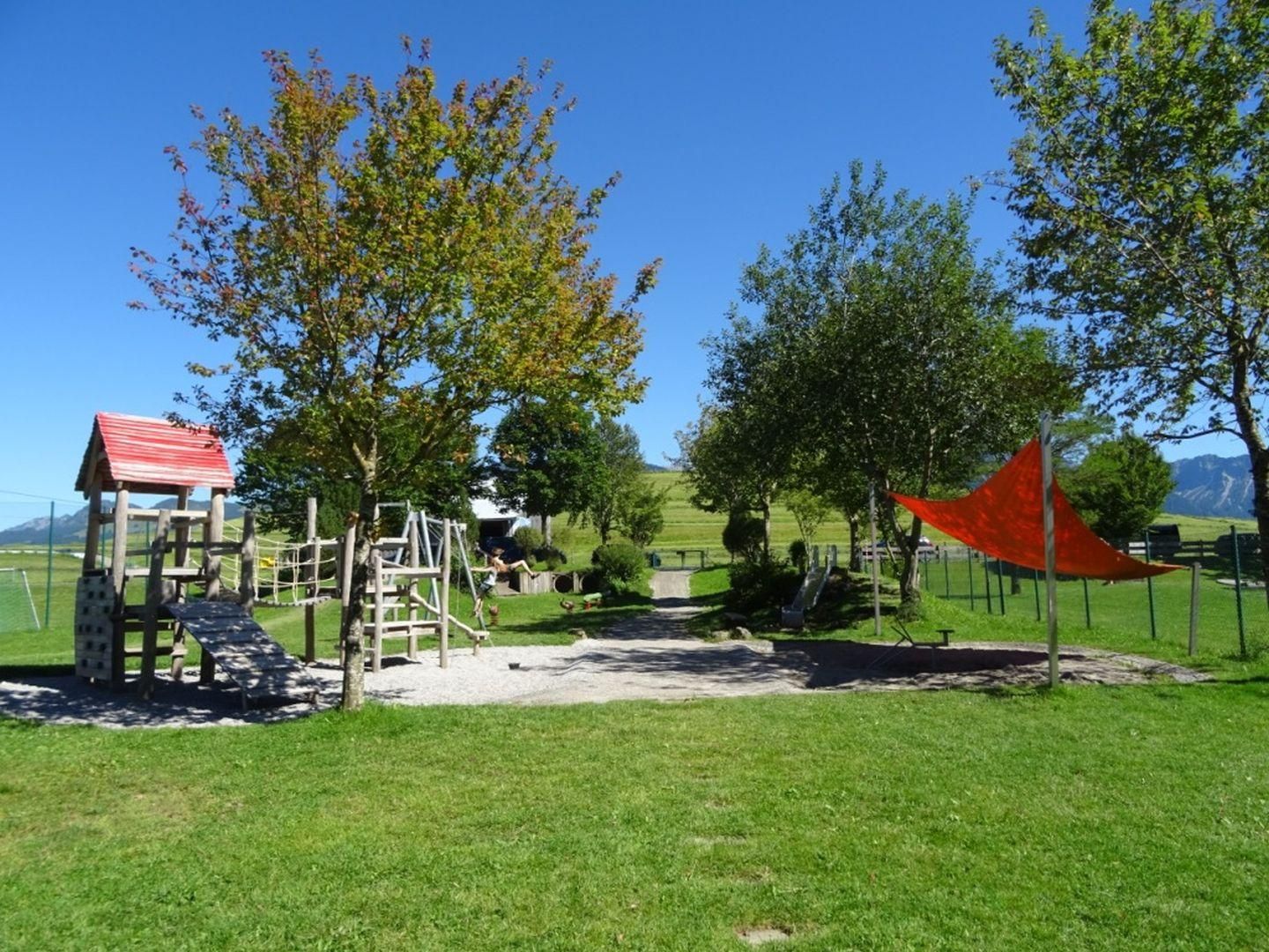 Spielplatz mit Rutsche, Klettergerüst, Schaukel und Sandkasten mit Sonnensegel.