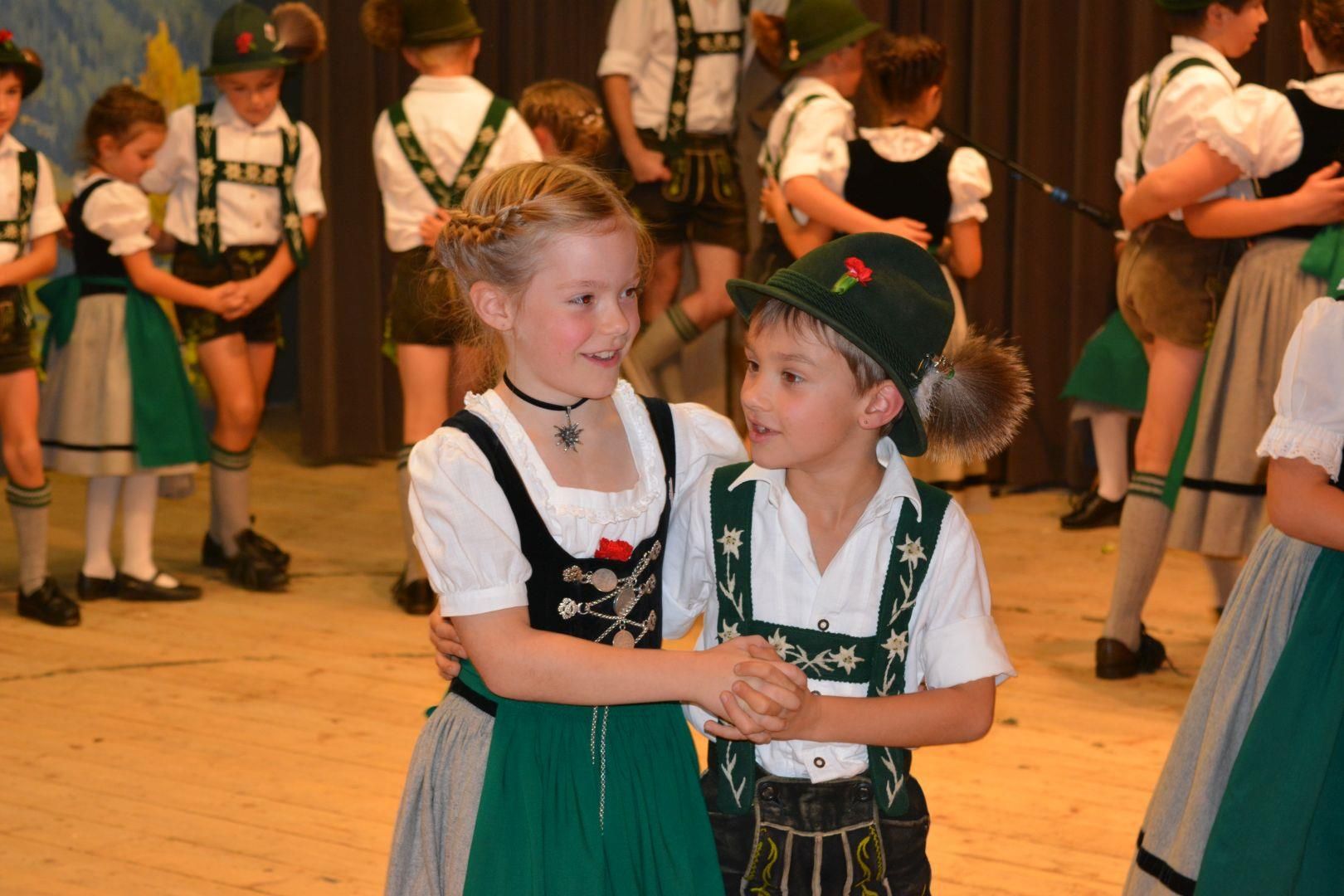 Heimatabend: Zwei Kinder in Tracht, ein Mädchen im Dirndl und ein Junge in Lederhose und Hut, tanzen.