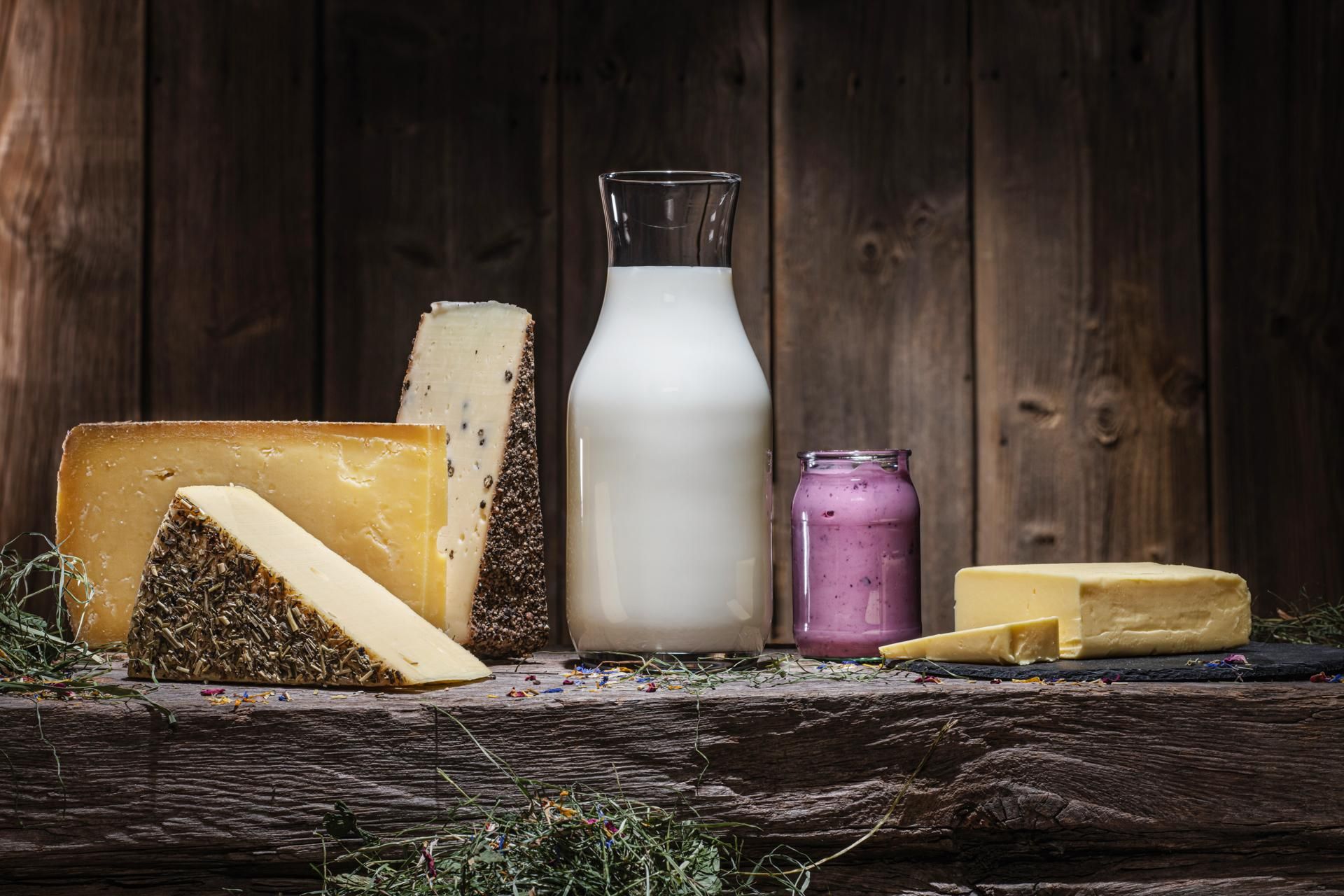 Verschiedene Milchprodukte (verschiedene Käsesorten, Milch, Joghurt, Butter) vor einer alten Holzwand.