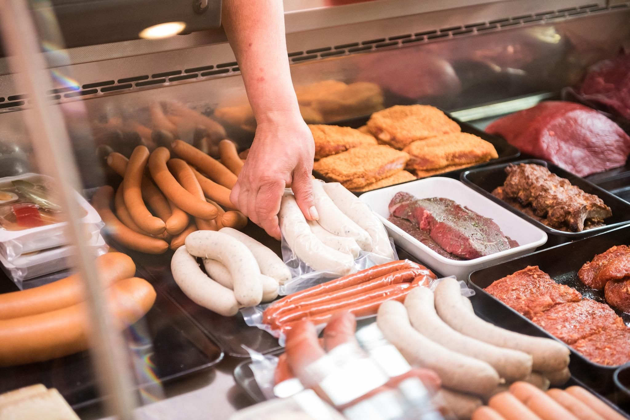 Eine Hand greift in eine Kühltheke und nimmt weiße Würste heraus
