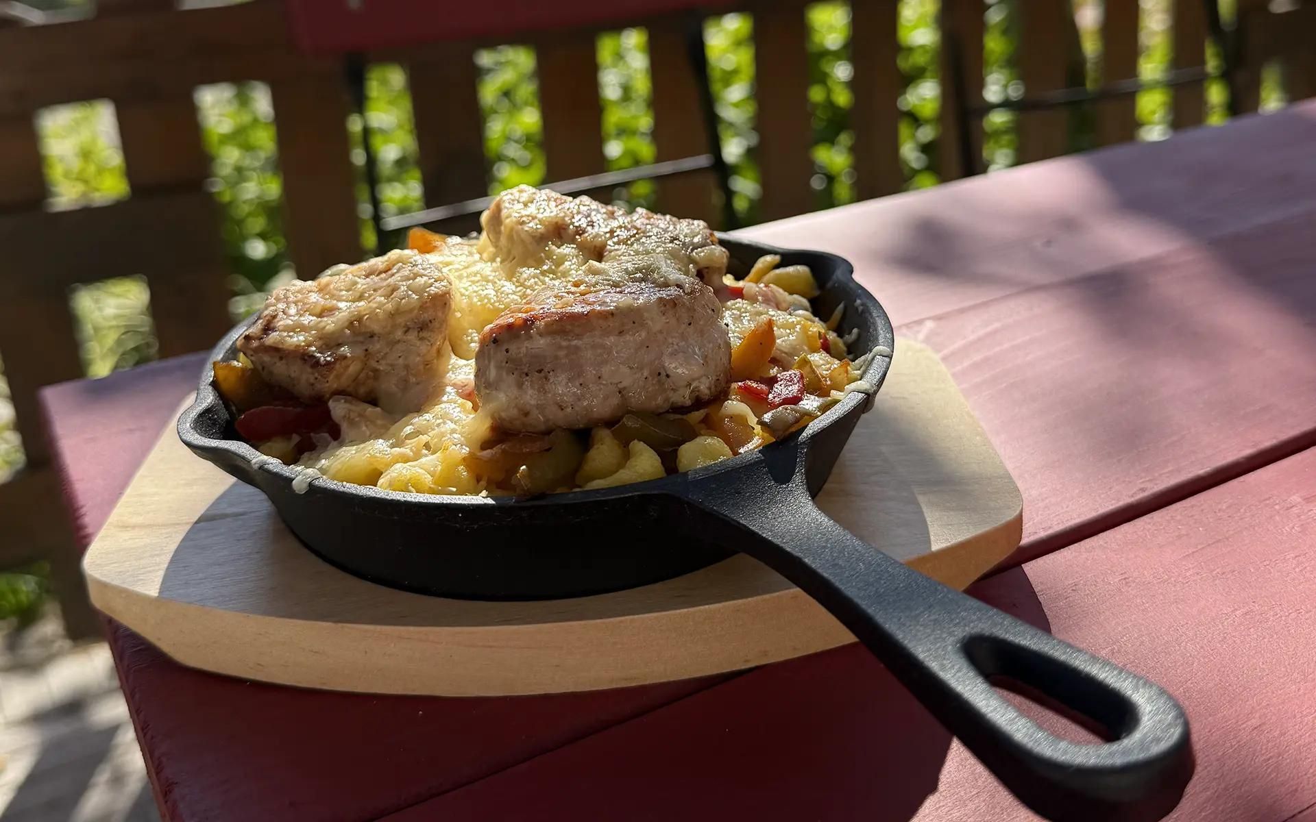 Sonneck-Pfännle, ein mit Bergkäse überbackenes Schweinefilet auf Spätzle mit Paprikasauce in einer kleinen Pfanne serviert auf einem Holzbrett.