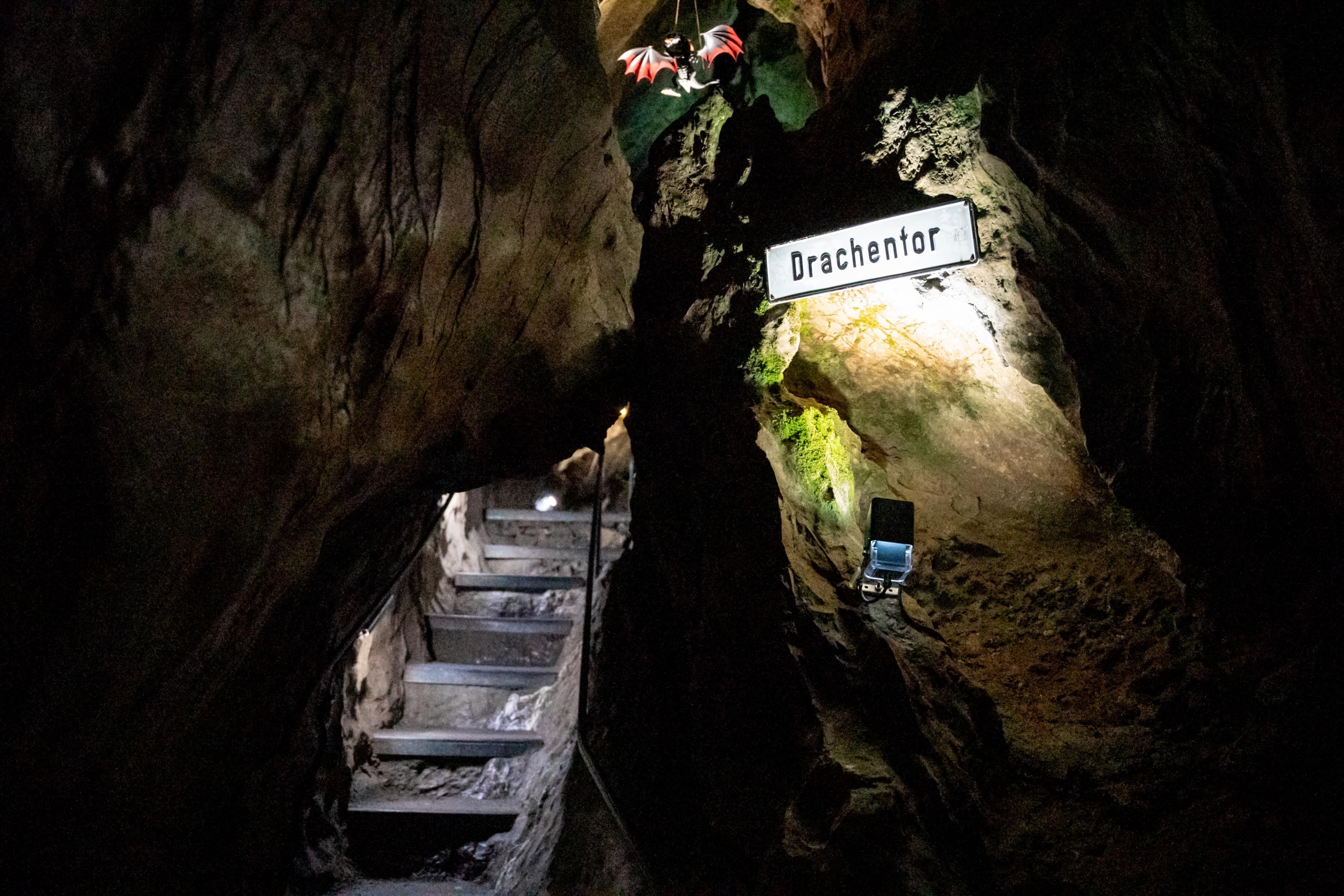 Stufen in einer leicht beleuchteten Höhle mit einem Schiöd weclhes die Aufschrift Drachentor enthält