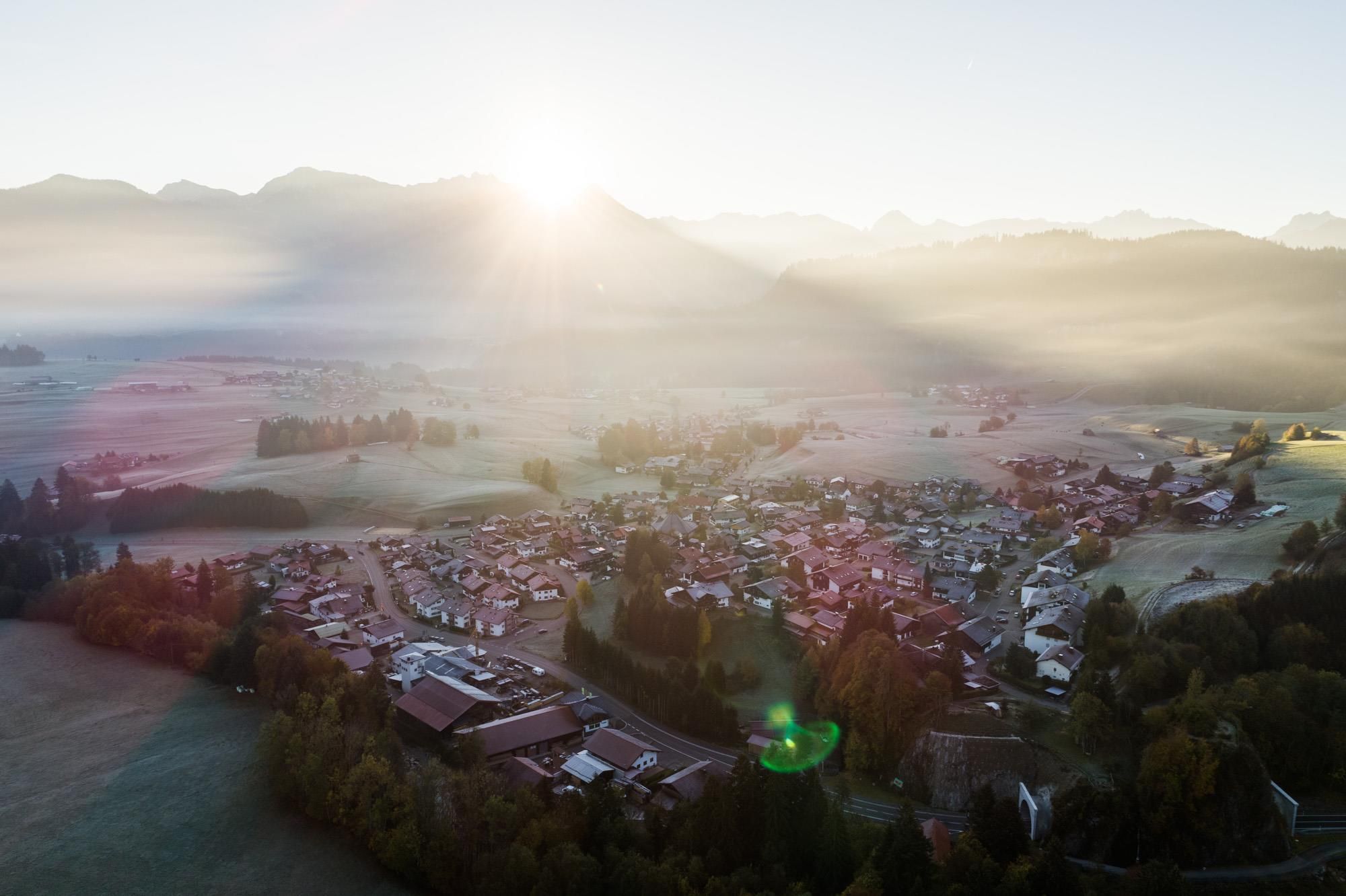 Luftaufnahme des Dorfes Obermaiselstein im Allgäu, eingebettet in grüne Hügel.