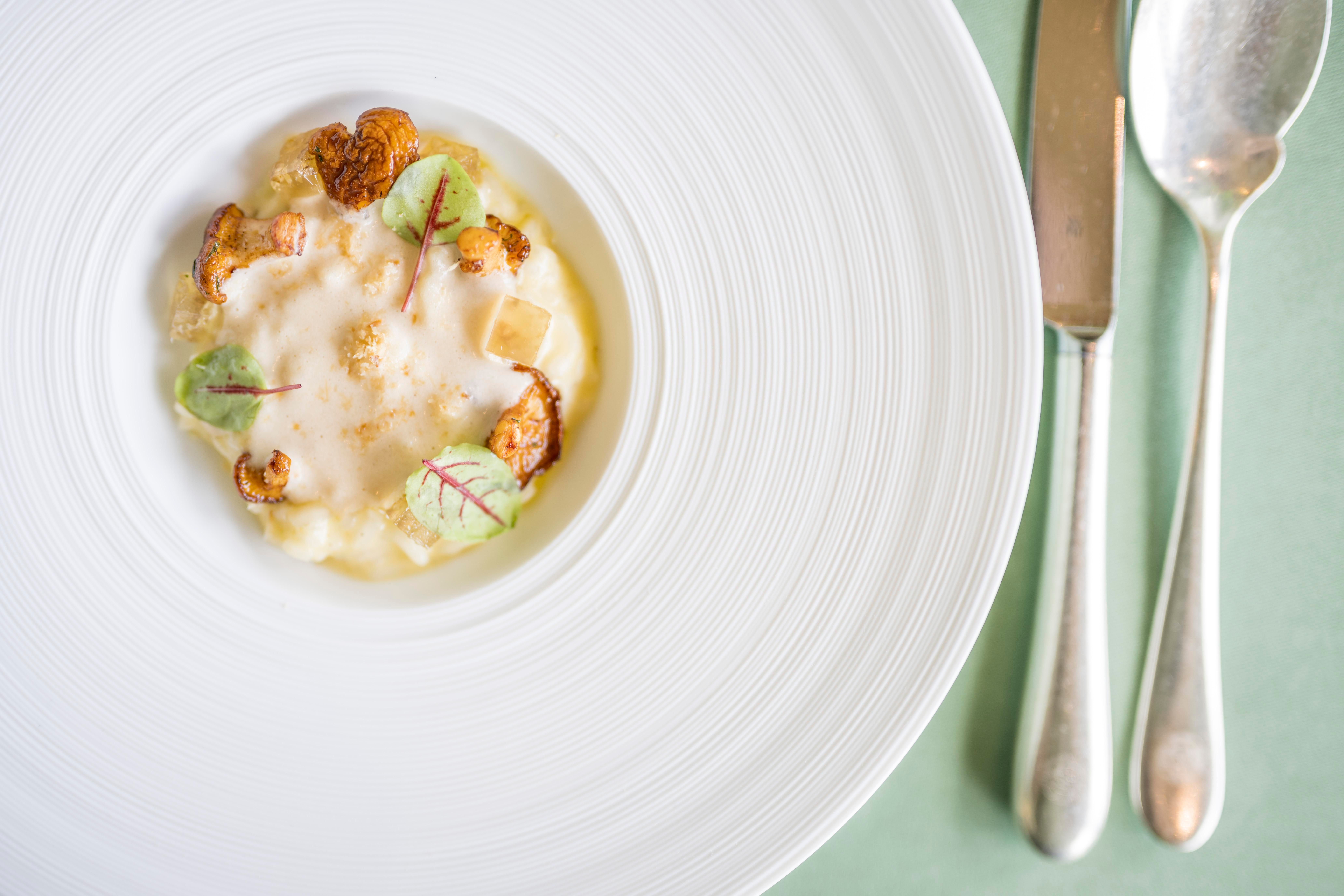 <p>Fein angerichteter weißer Teller auf blauer Unterlage. Daneben liegen Löffel und Messer.</p>