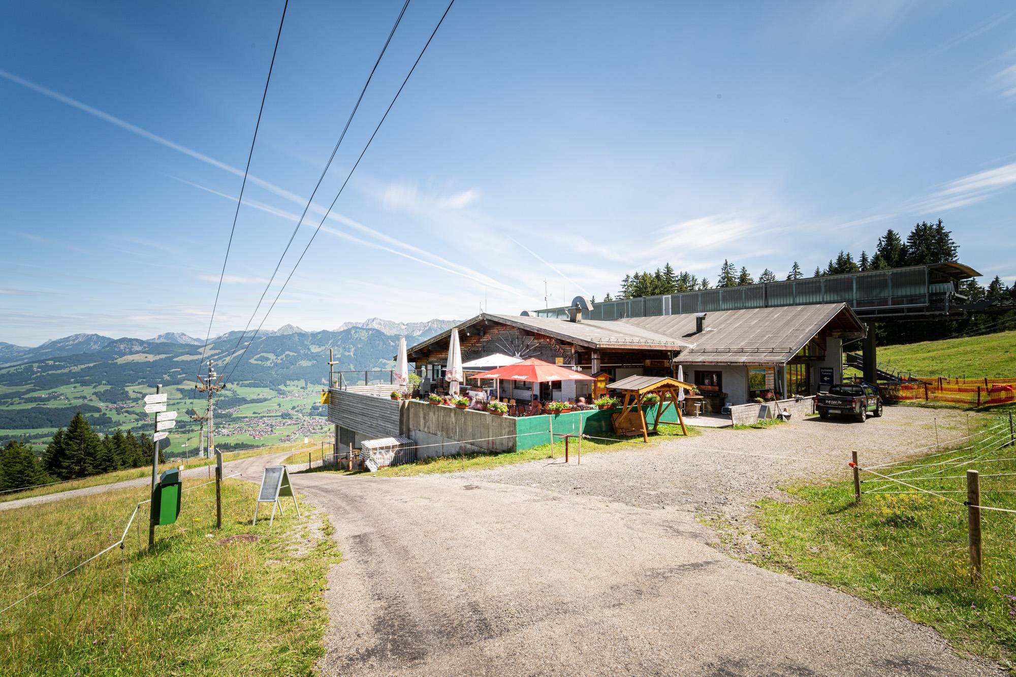 Das "s`Mibbadin" an der Hörnerbahn Mittelstation. Ein Schotterweg führt zum Gebäude. Im Hintergrund eine grüne Berglandschaft.