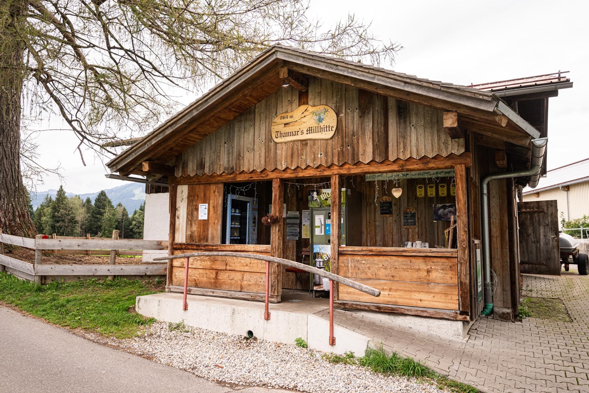 Blockhaus mit Holzverkleidung und der Aufschrift "Thanner's Müllhitte" an einem Weg.