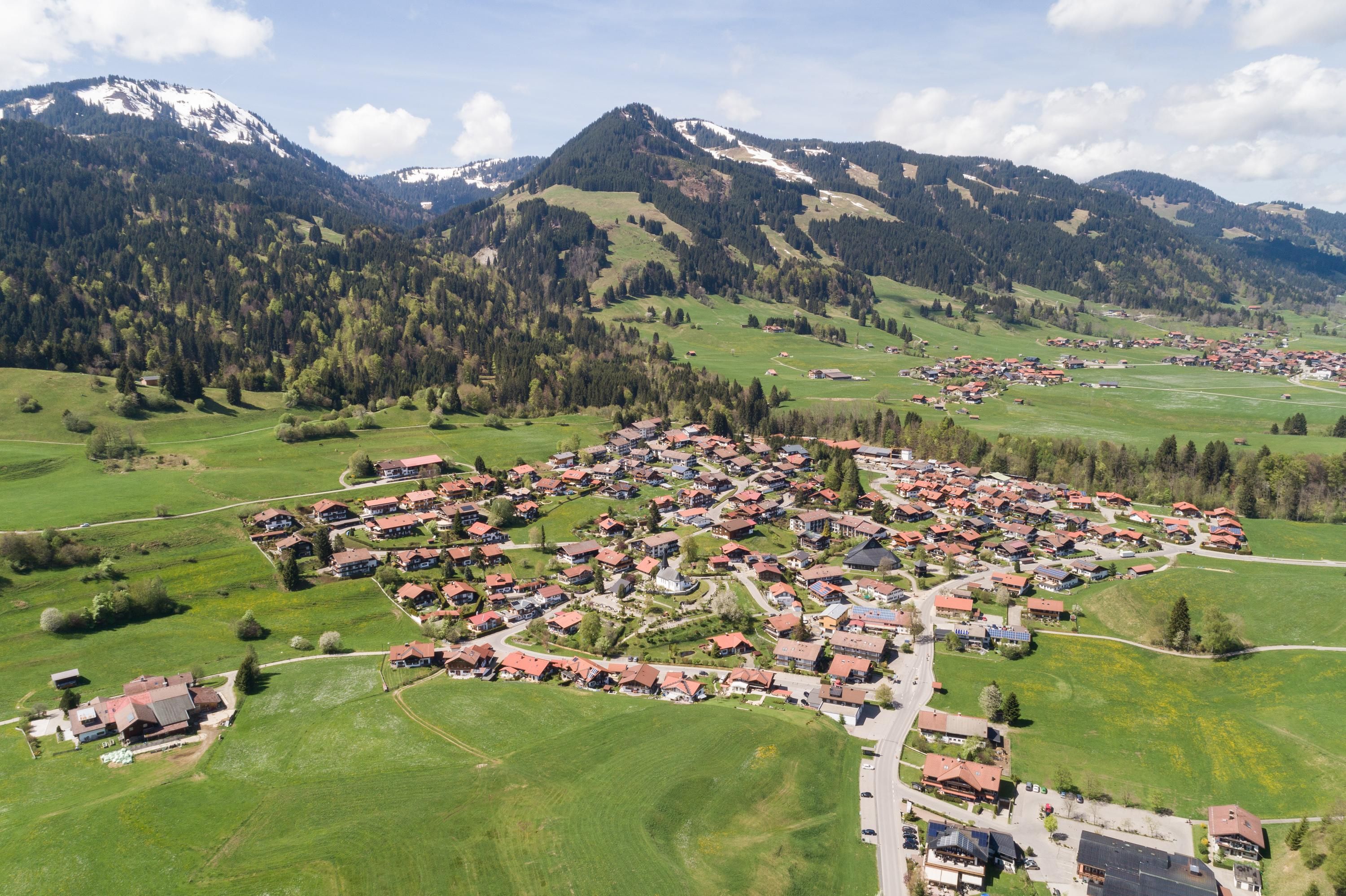 Luftaufnahme von Obermaiselstein, einem Dorf eingebettet in eine grüne Berglandschaft.