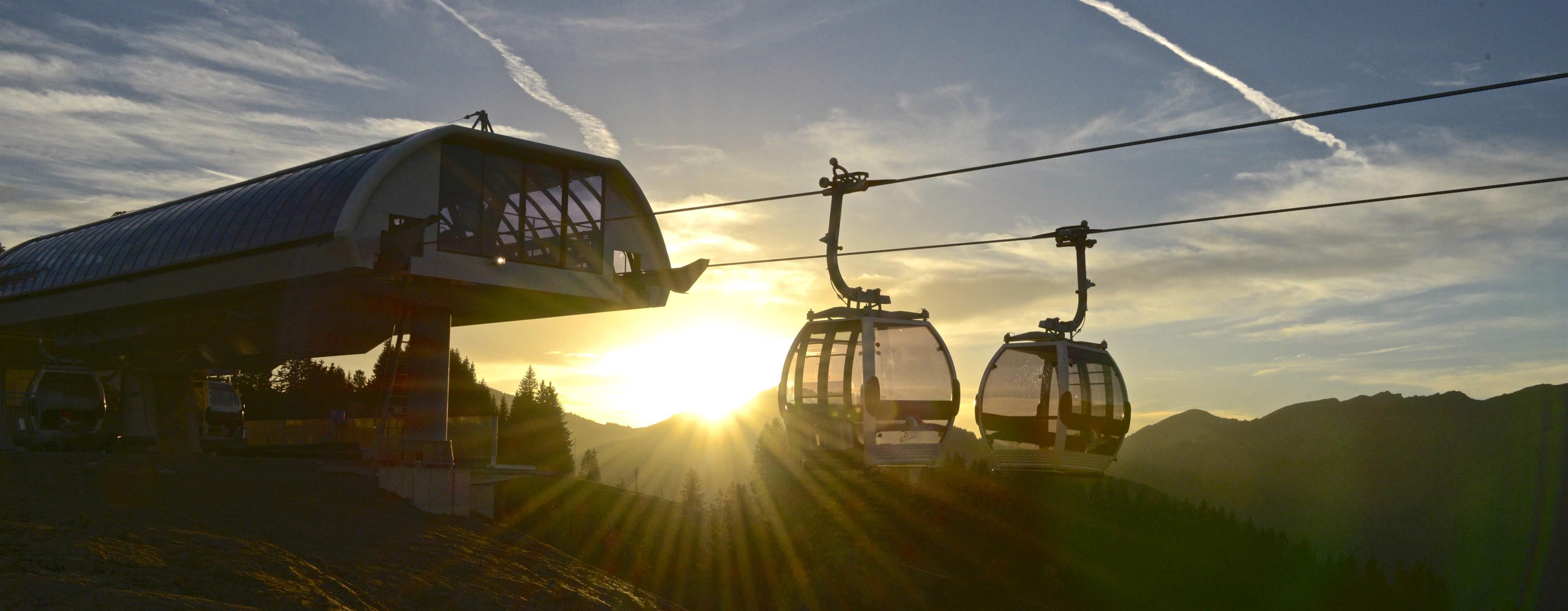 Sonniger Sonnenuntergang über der Ossi-Reichert-Bahn. Zwei Gondeln und Bergstation, Berge im Hintergrund.