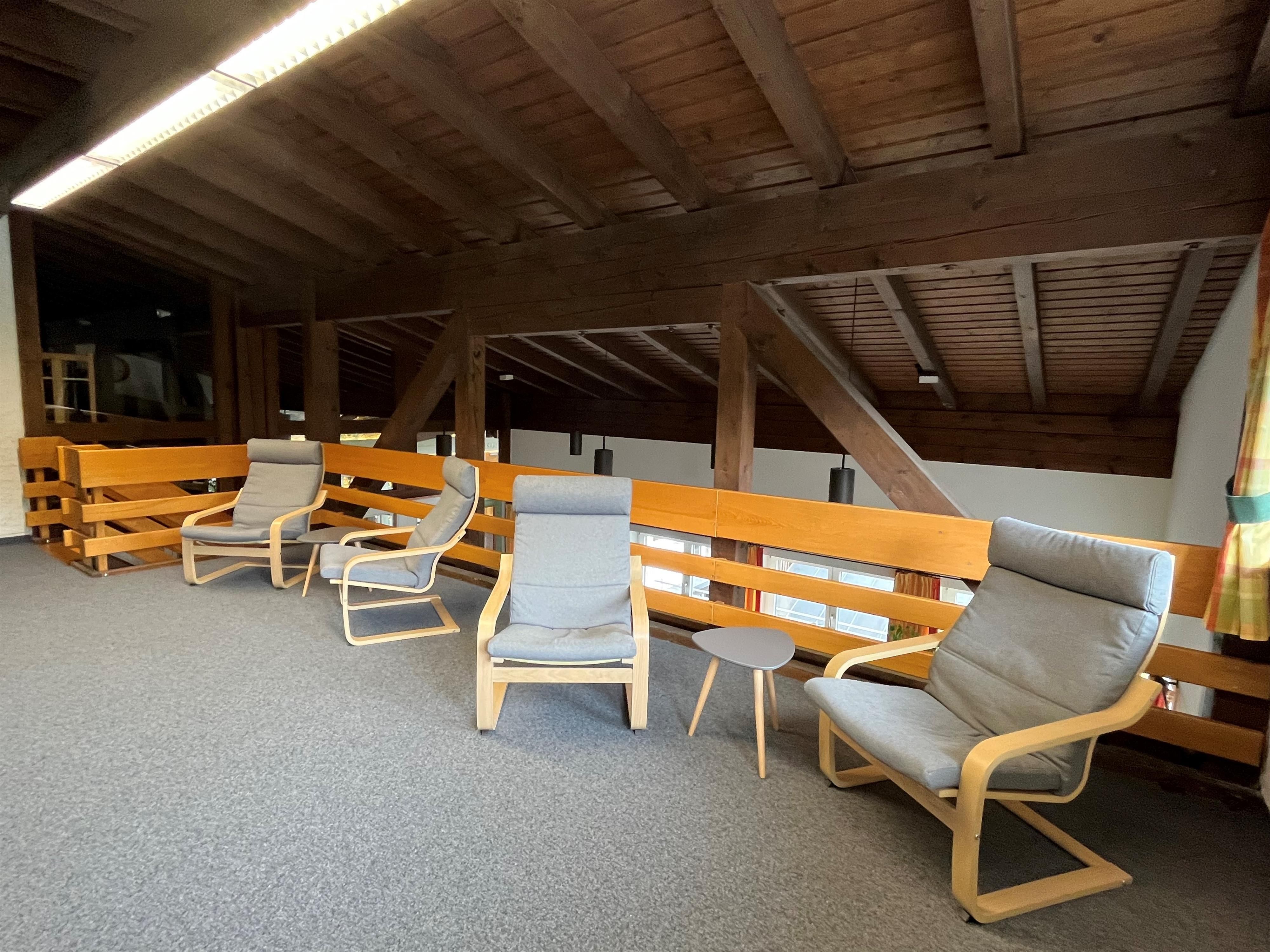 Lesebereich in der Gemeindebücherei Obermaiselstein. Gemütliche graue Sessel mit Holzelementen stehen auf einem grauen Teppichboden.