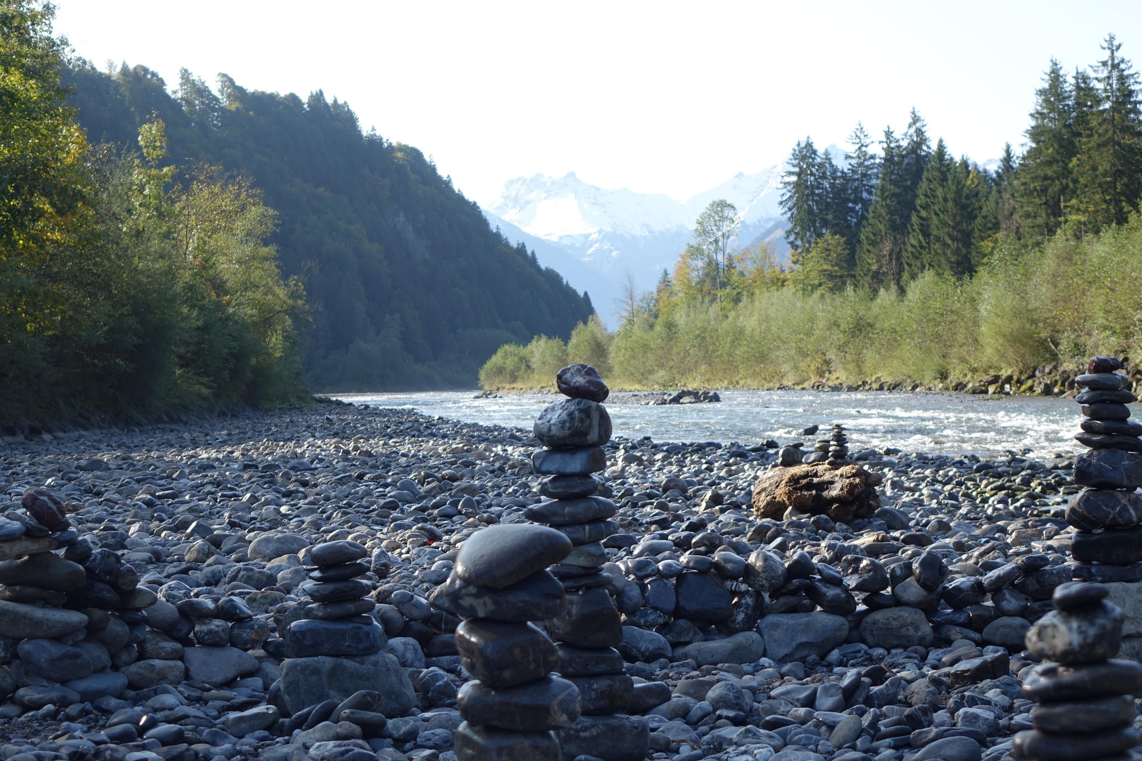 Ein Steinmännchen aus gestapelten Steinen, das an einem Fluss steht, am anderen Ufer Weidenbäume.