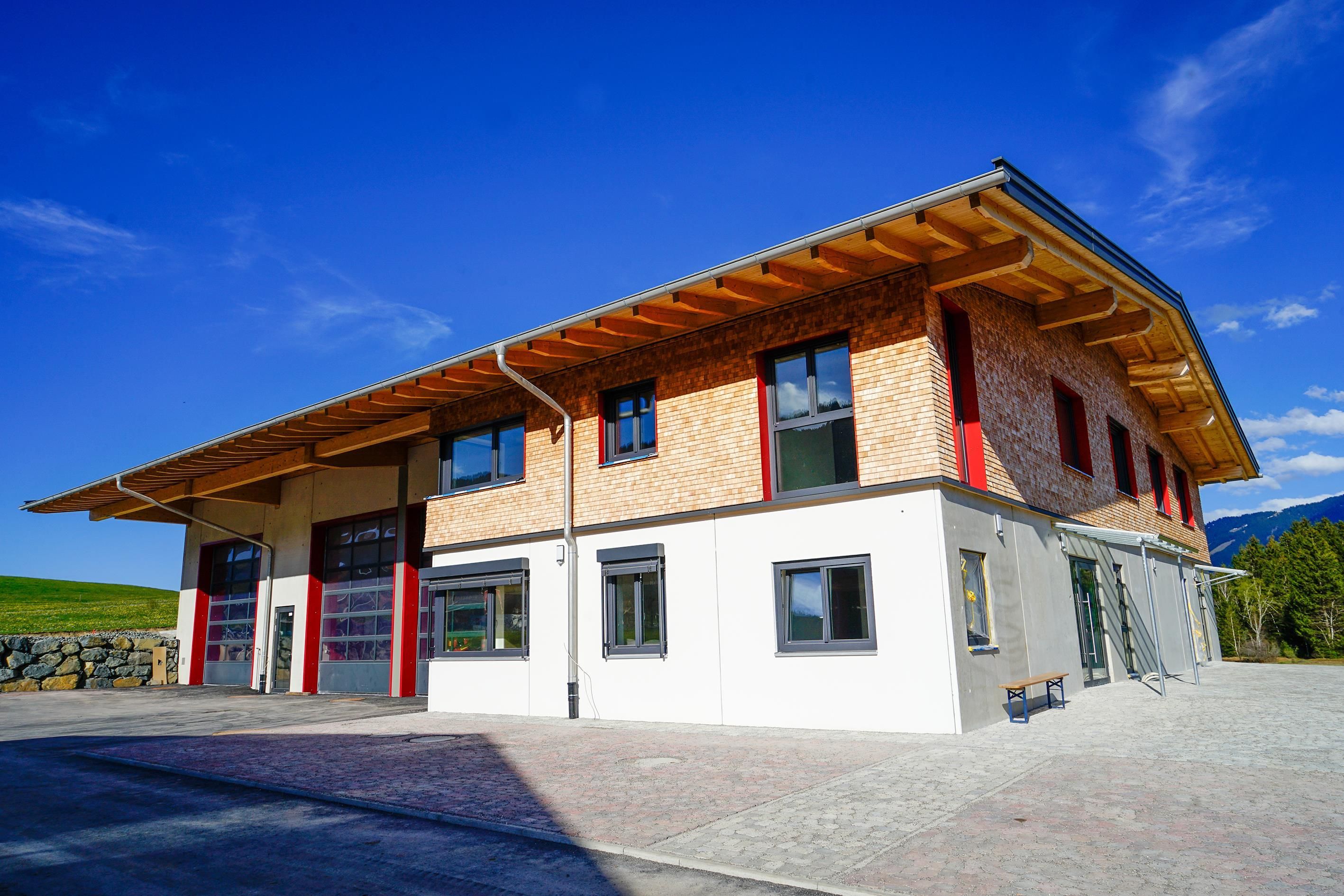 Ein großes, modernes Haus steht auf einem gepflasterten Platz. Direkt nebenan ist eine Maschinenhalle mit großen Toren.