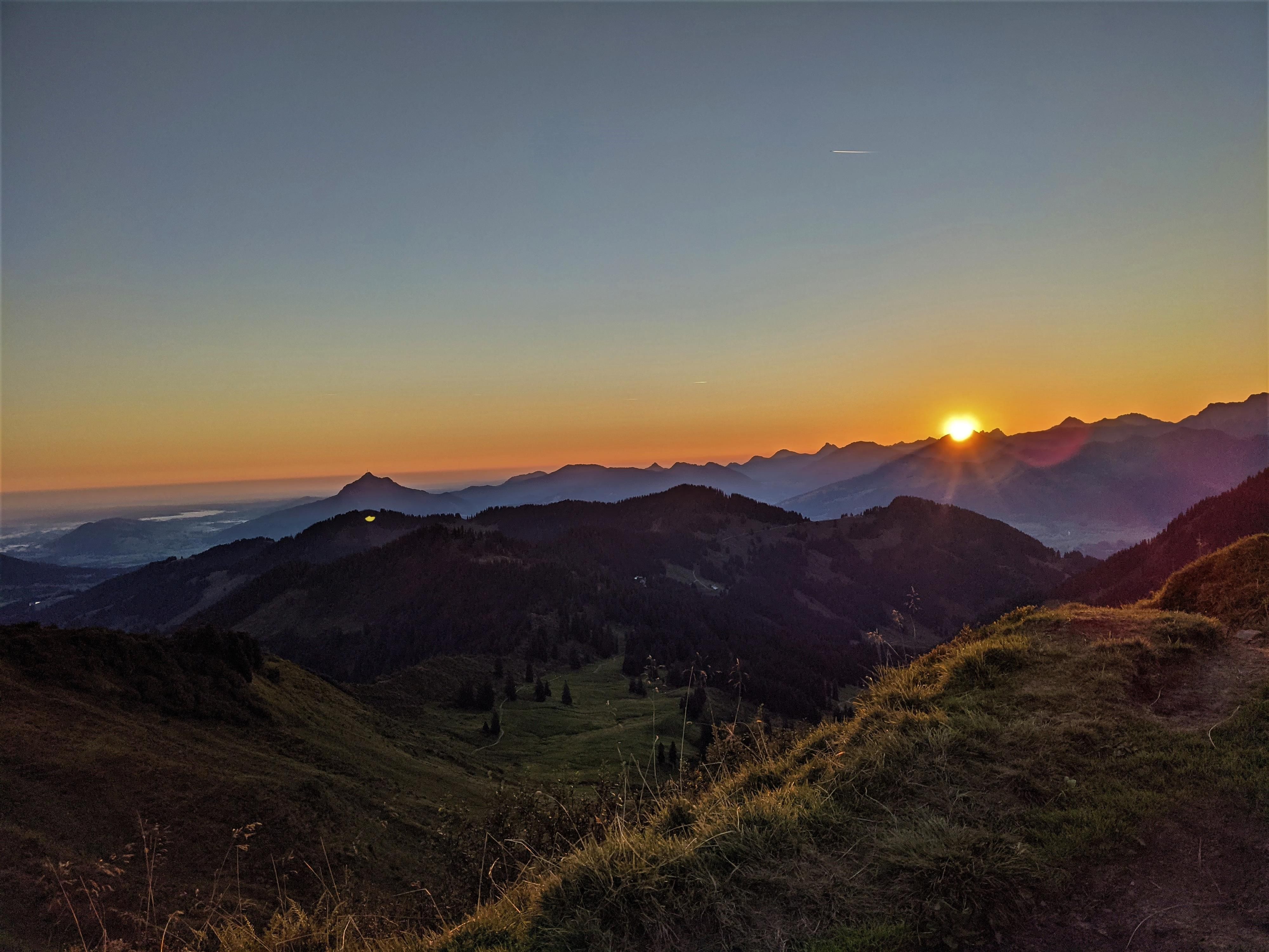 Weitläufiges Bergpanorama bei Sonnenaufgang. Mehrere Bergketten erstrecken sich über den Horizont.