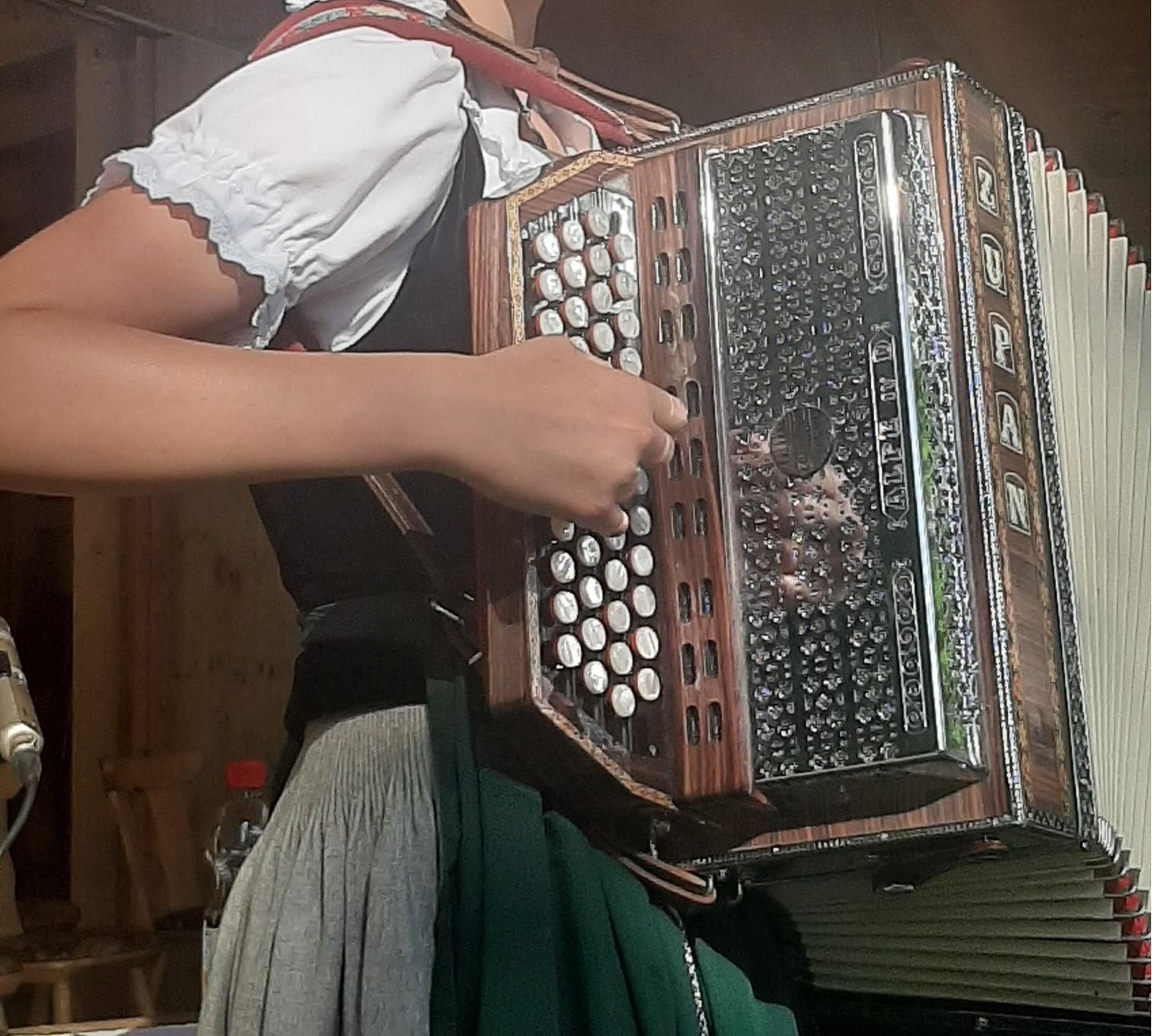Detailaufnahme einer Person in Tracht, die ein Akkordeon spielt. Die Hände bedienen die Knöpfe und den Balg.