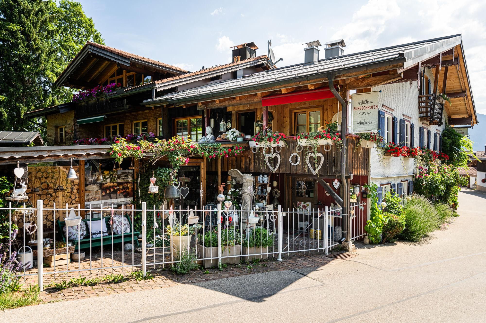 Mehrstöckiges Landhaus Burgschrofen in Obermaiselstein. Holzverkleidung und dunkles Dach. Balkone mit roten Blumenkästen.