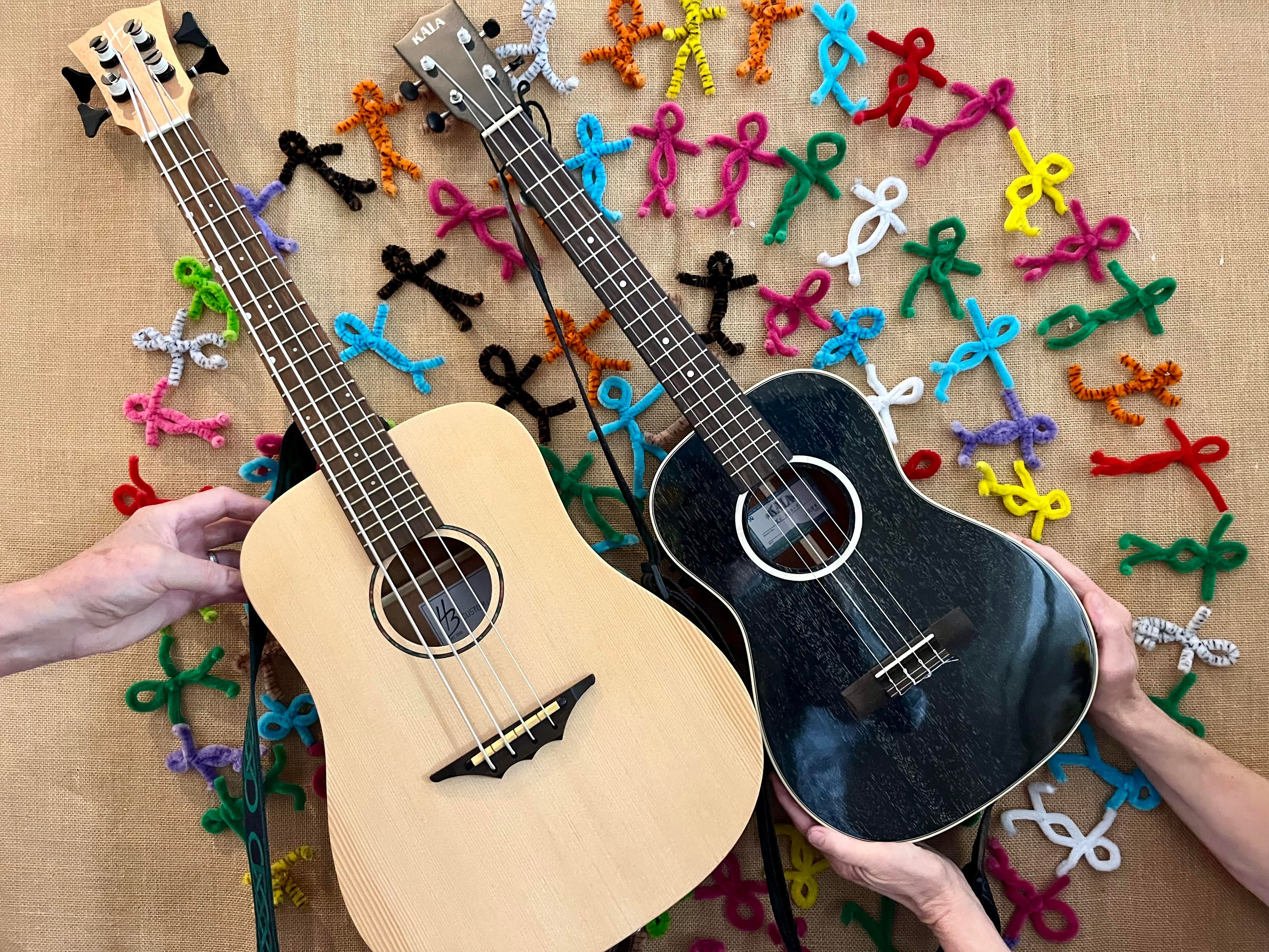 Zwei Ukulelen werden gehalten. Im Hintergrund sind bunte, handgemachte Figuren aus Pfeifenreinigern zu sehen.