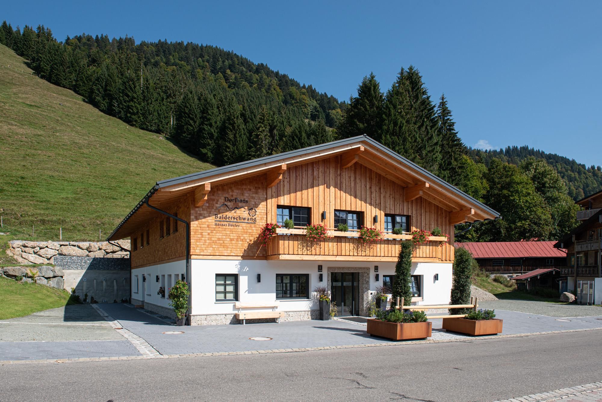 Dorfhaus Balderschwang, ein zweistöckiges Gebäude mit Holzfassade im Obergeschoss und weißem Putz darunter. Dunkles Satteldach.