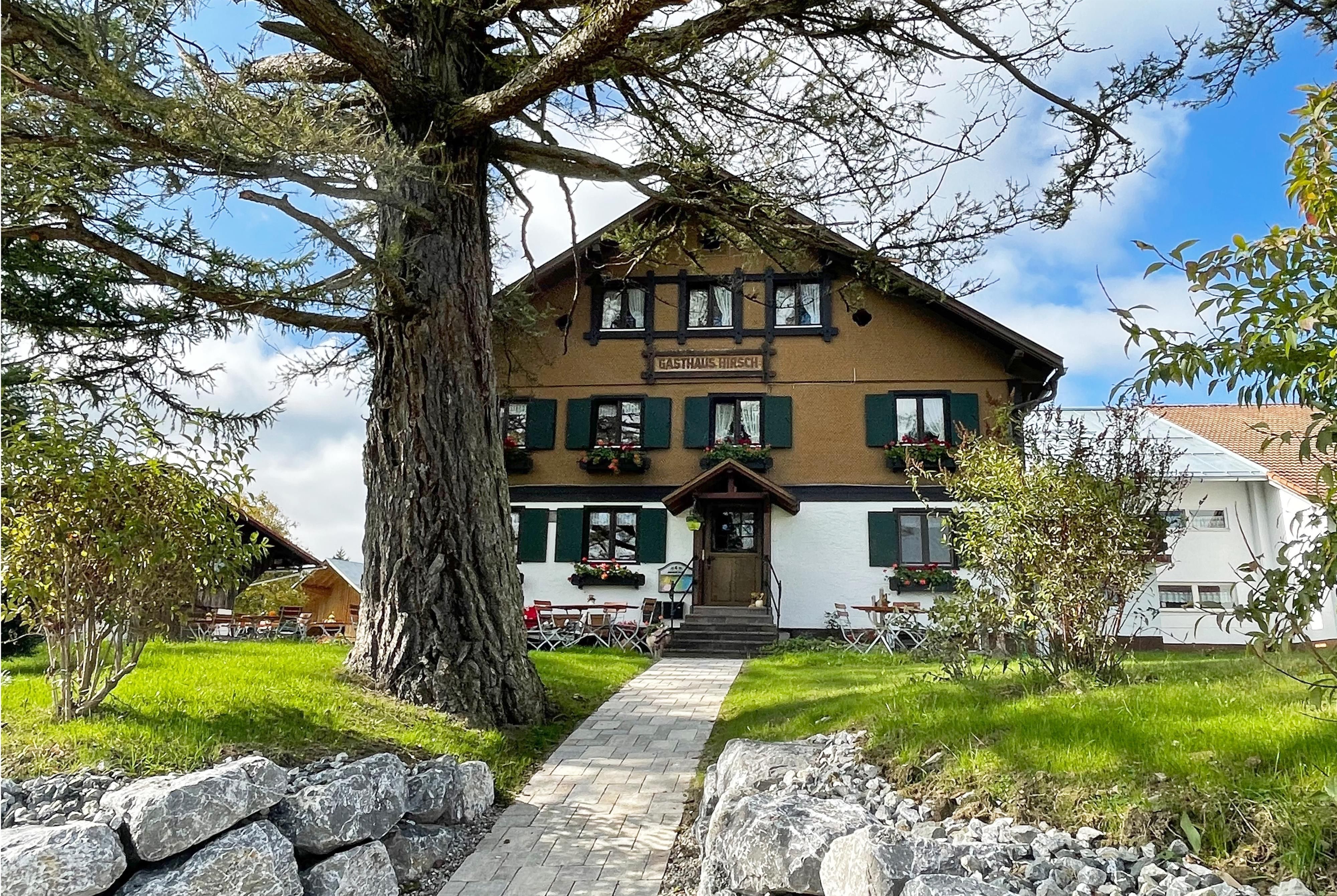 Gasthaus Hirsch, zweistöckiges Gebäude, braune Fassade, weiße Akzente, grüne Fensterläden, "Gasthaus Hirsch" Schild über dem Eingang.