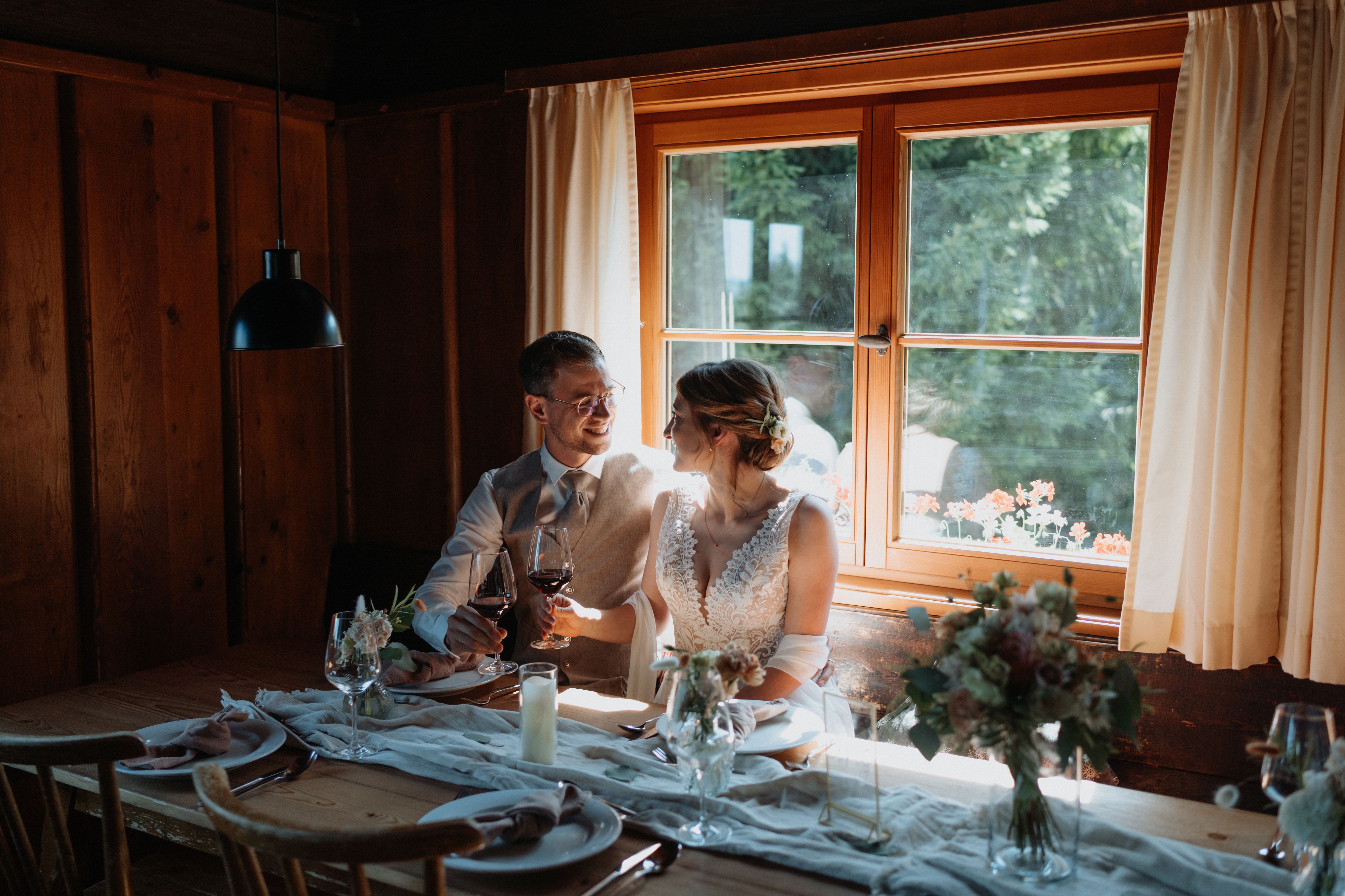 Bautpaar an gedecktem Hochzeitstisch, dahinter uriges Holzfenster mit Gardinen