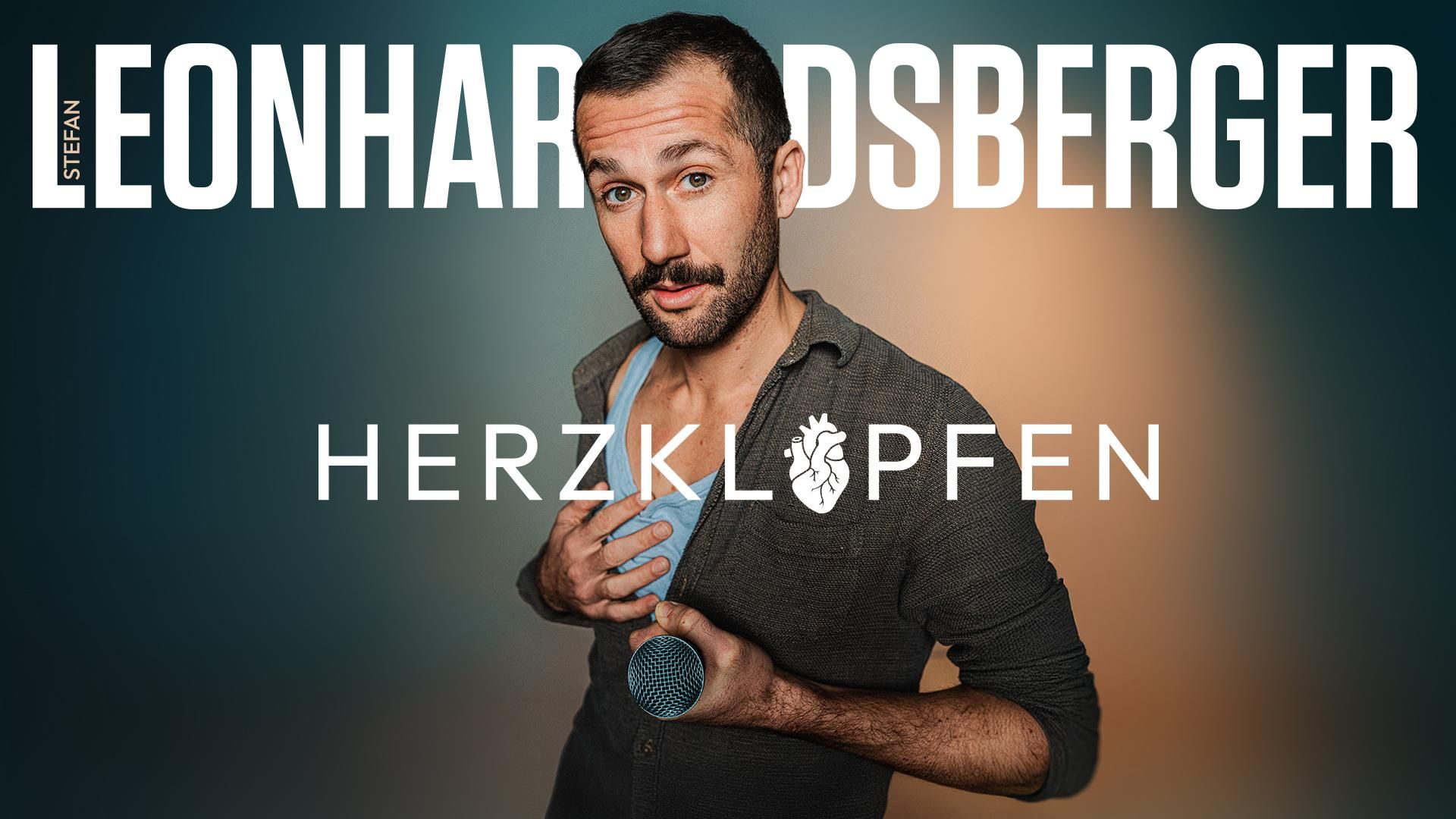 Kabarettist Stefan Leonhardsberger als Portrait -  mit Mikrofon in der Hand und einer Hand auf dem Herzen - für sein Programm Herzklopfen
