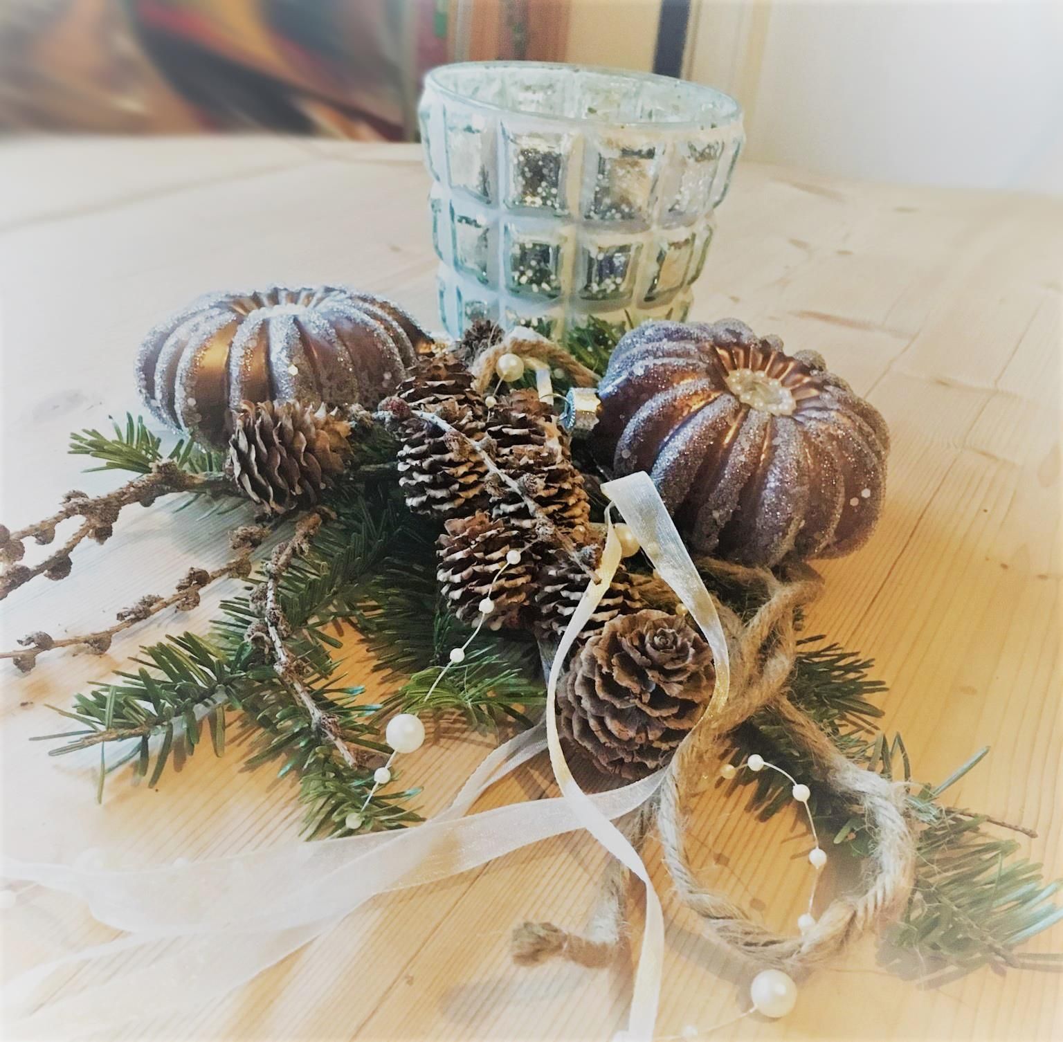 Eine selbstgemachte Dekoration mit kleinen, künstlichen Kürbissen, Tannenzapfen und Schleife, dahinter ein Teelicht.