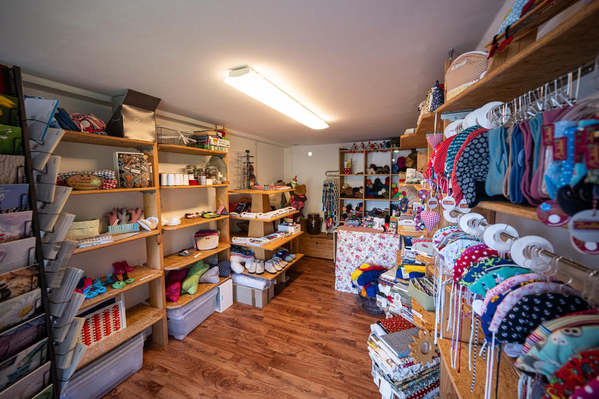 Ein kleiner Ladenraum mit Holzregalen voller Waren an hellen Wänden und Holzboden.
