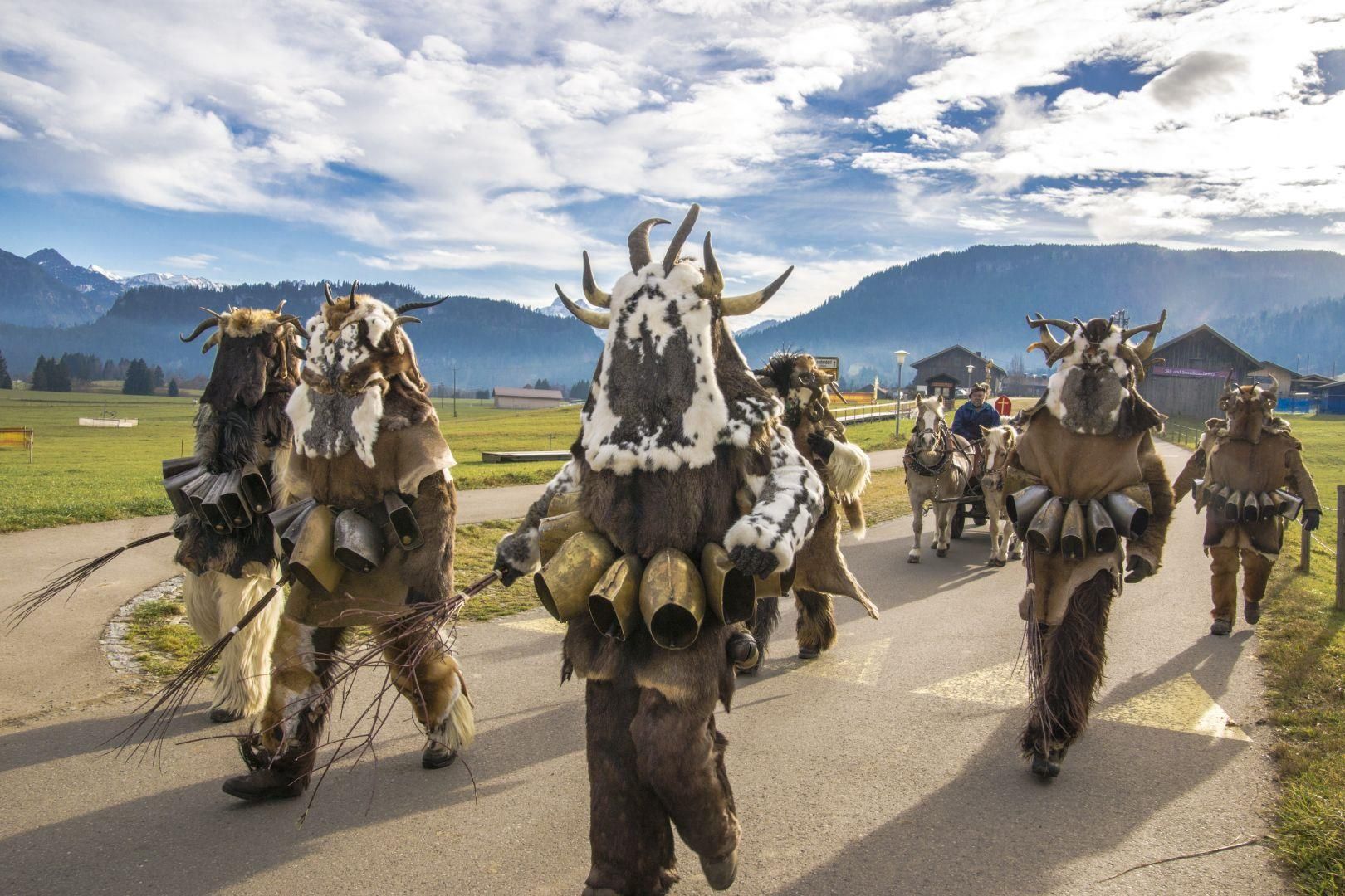 Gruppe von fünf Krampusse in Fellkostümen mit Hörnern und Glocken, die auf einer Straße gehen.