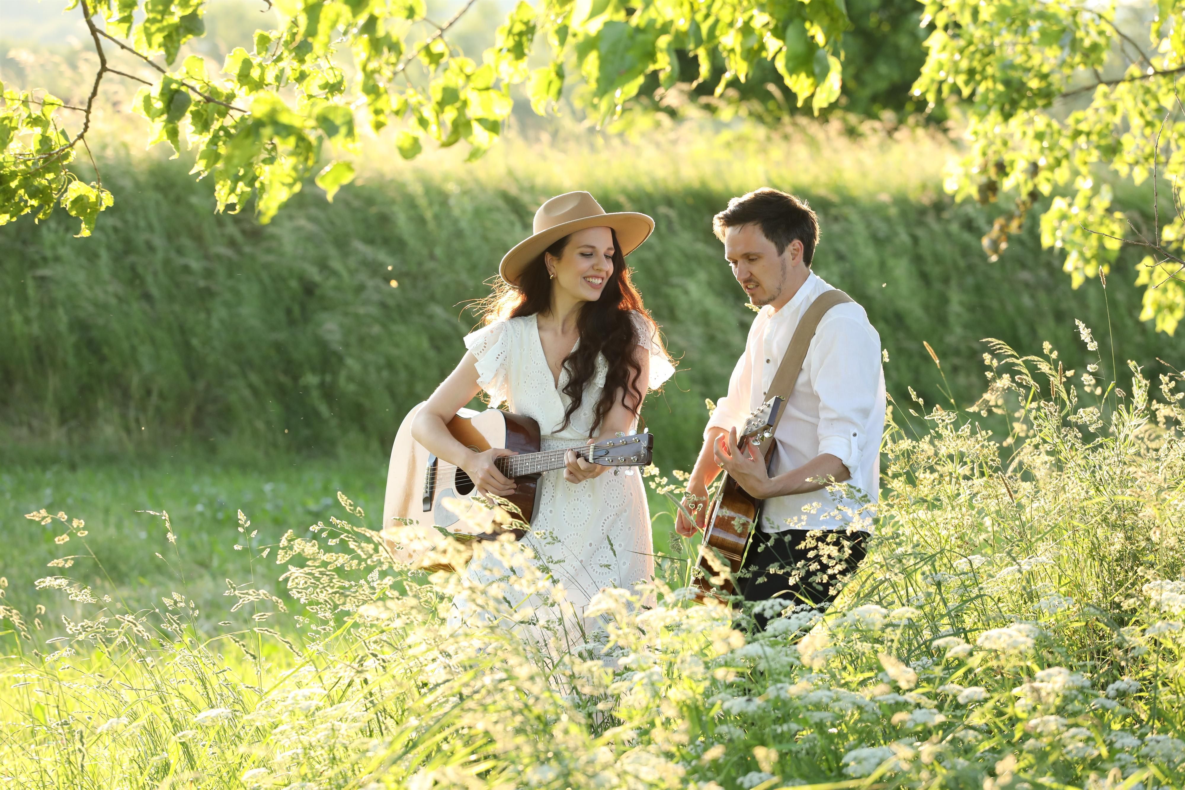 Das Duo Man n Maid - bestehend aus Doreen Brunner und Tobi Dorn - beide in weiß gekleidet mit ihren Gitarren um den Hals in mitten einer grünen, saftigen Wiese.