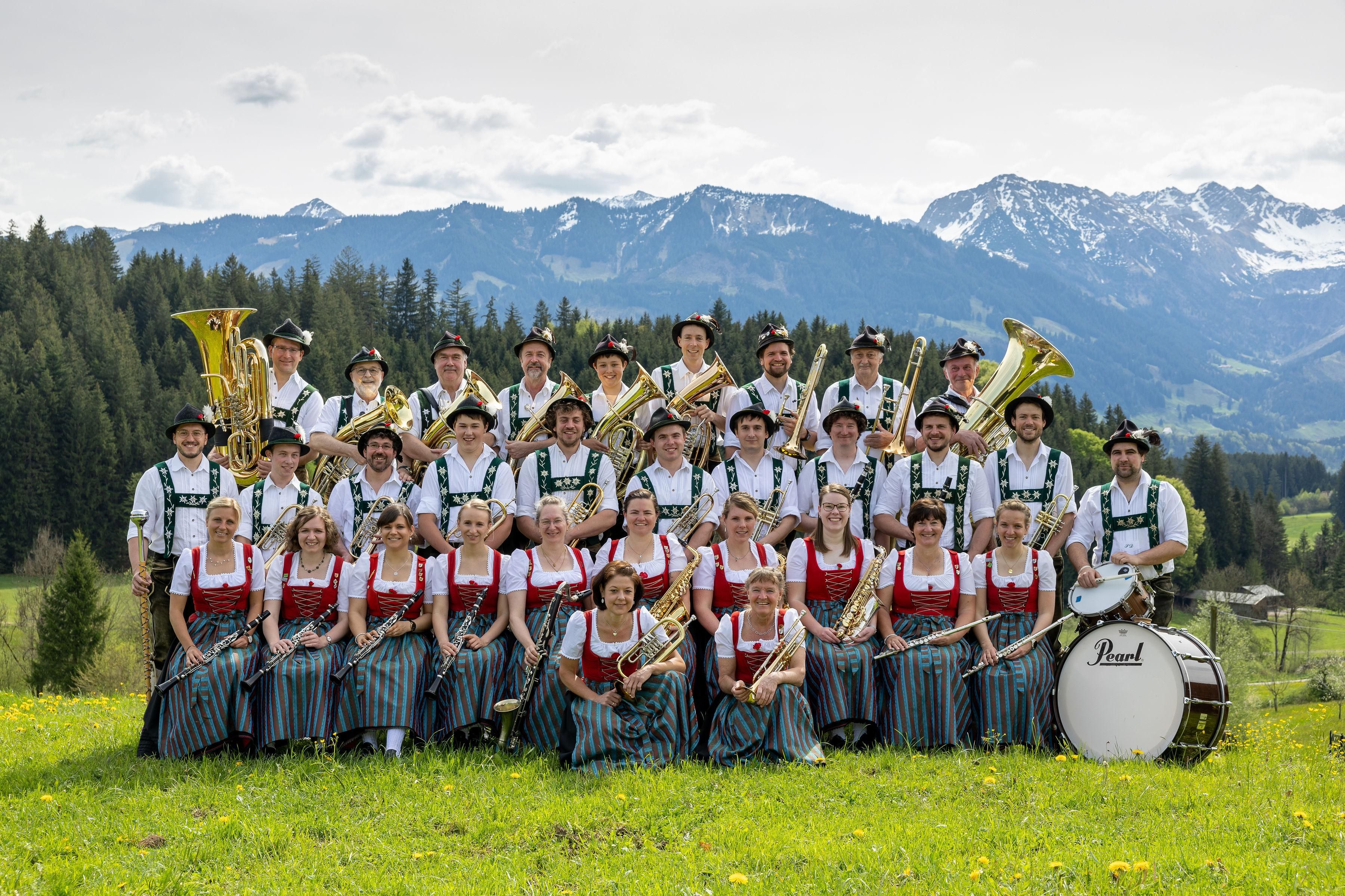 Die Musikkapelle Bolsterlang posiert in Tracht mit Instrumenten auf einer Wiese vor einer Bergkulisse.