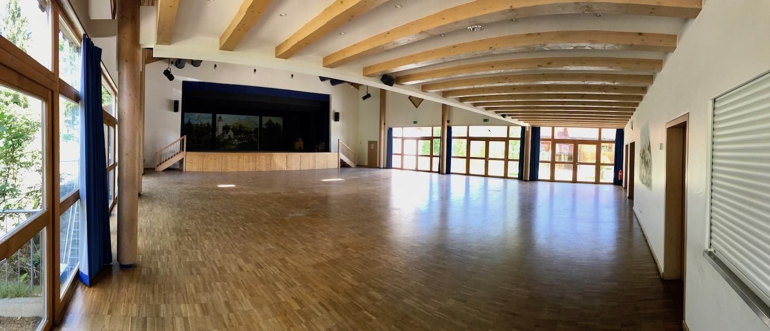 Großer Festsaal im Ofterschwanger Haus mit Bühne und großer Fensterfront auf zwei Seiten des Saales.