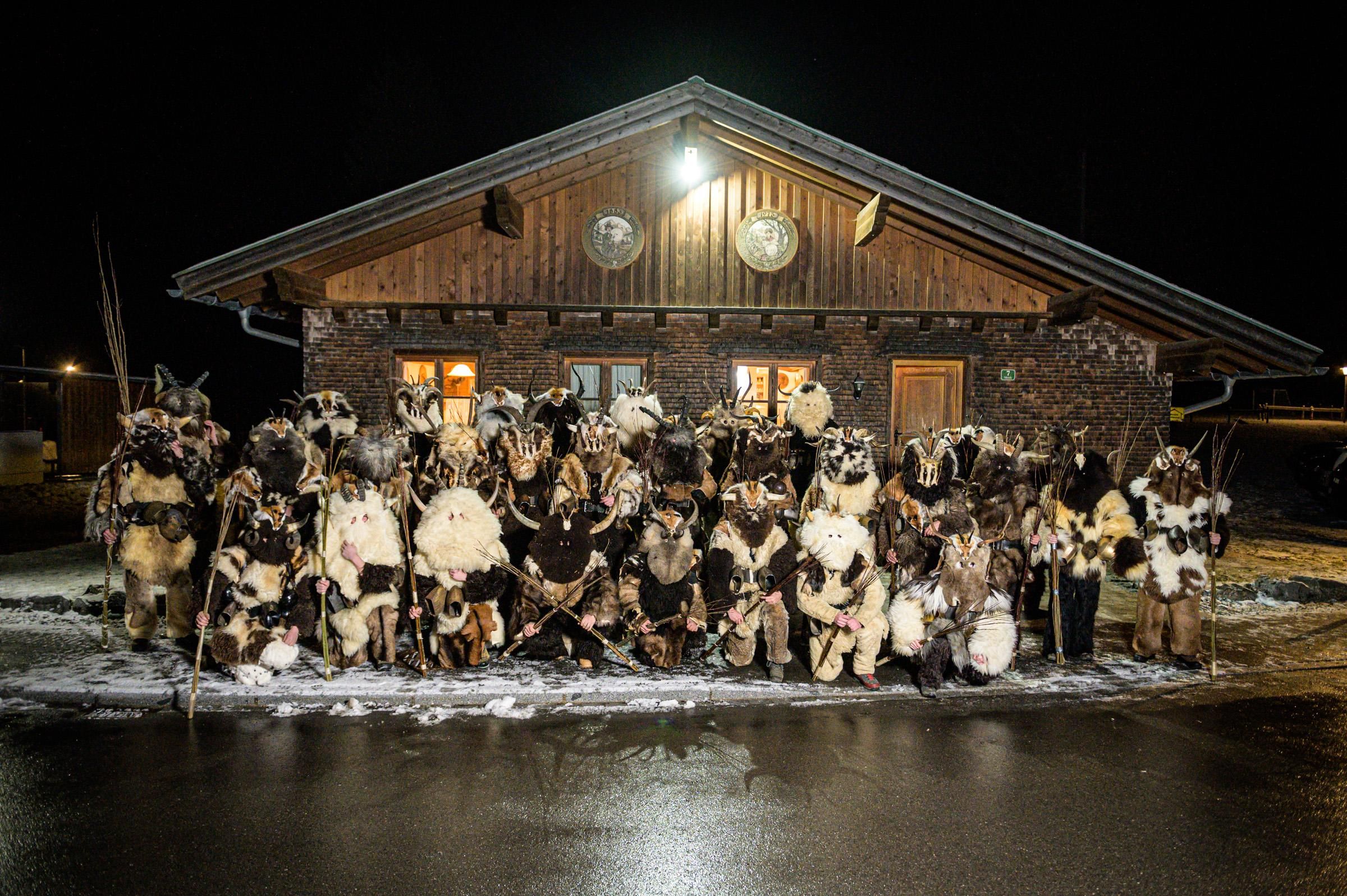 Viele Klausen in zotteligen Fellen vor einem Holzhaus. Sie tragen Hörner und Masken.