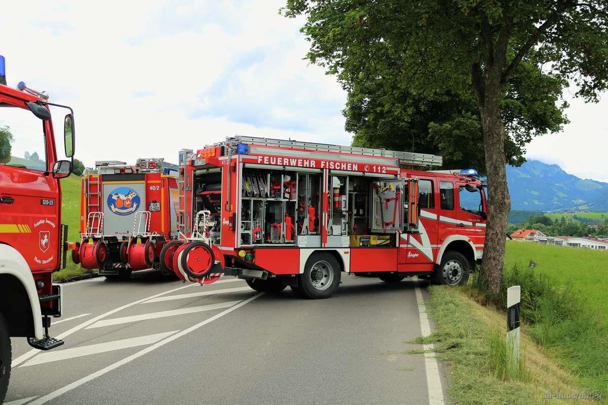 Feuerwehrautos bei einer Übung auf einer Straße, rechts eine Baumallee.